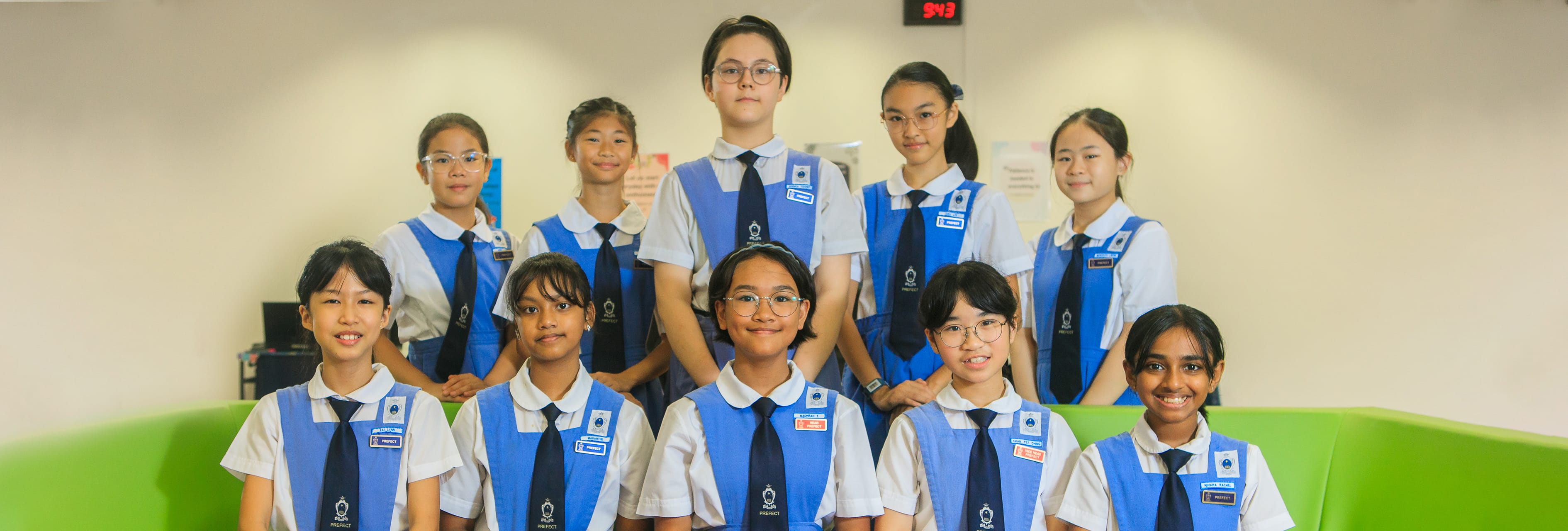 Ten schoolgirls in blue and white uniforms with ties pose in two rows indoors.