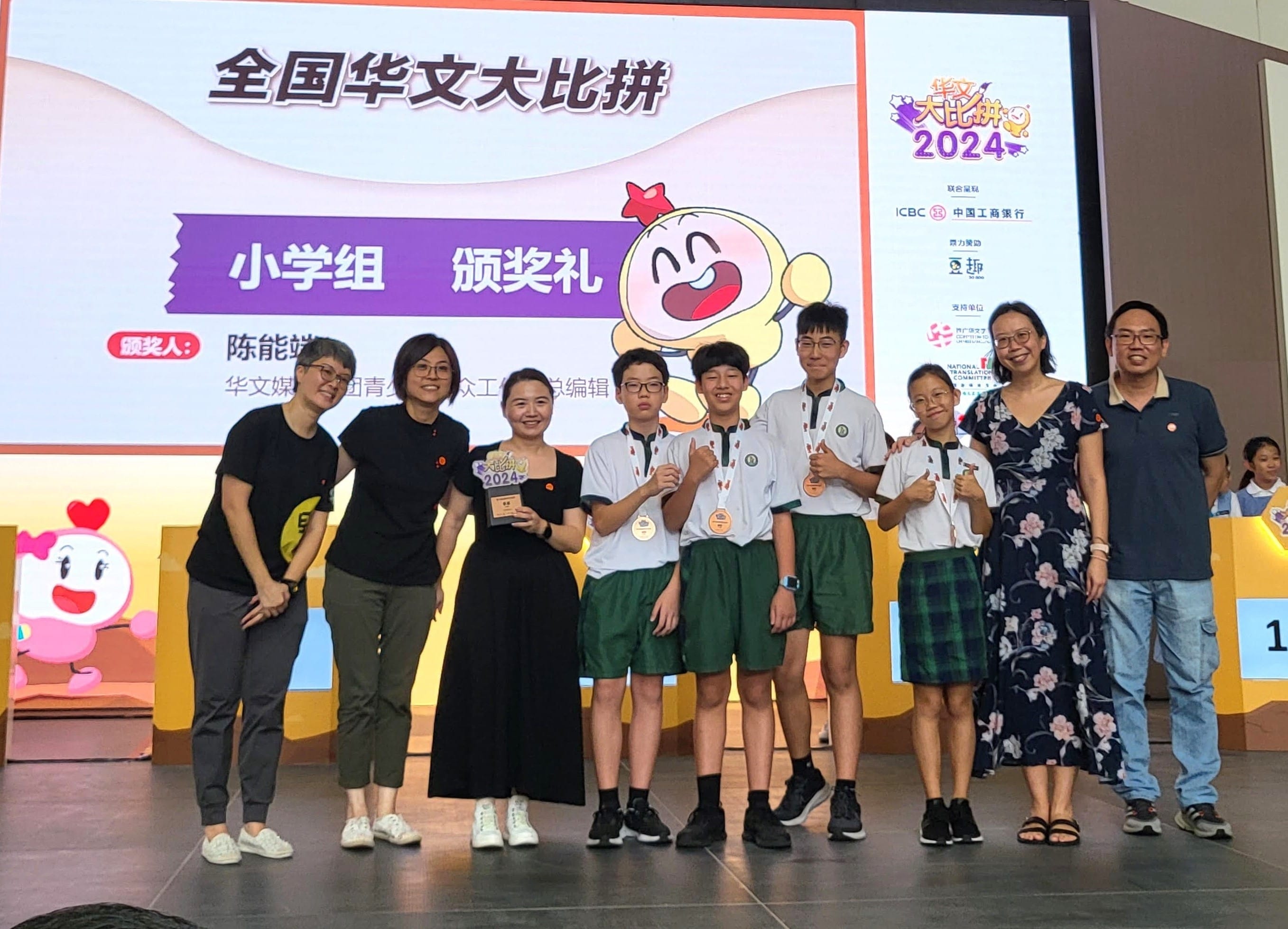 Group of students with medals and adults pose on stage at a 2024 Chinese language competition award ceremony.