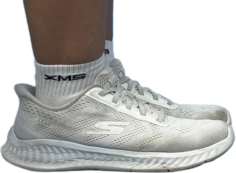 A person wearing a white Skechers Slip-Ins sneaker with gray laces and a white ankle sock labeled XMB.