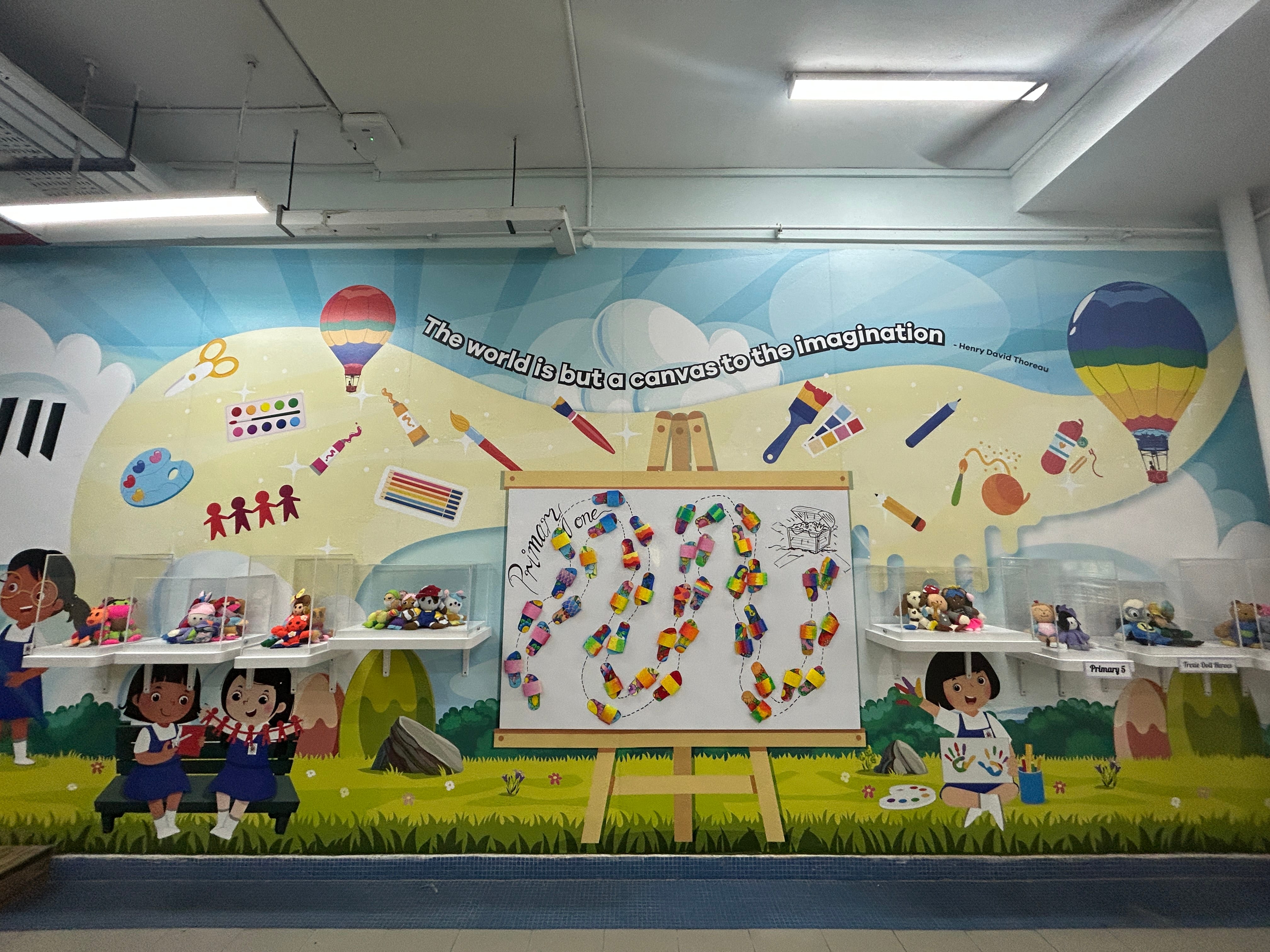 Colorful school mural with art tools and hot air balloons, quote by Thoreau, shelves of toys, and an easel with artwork.
