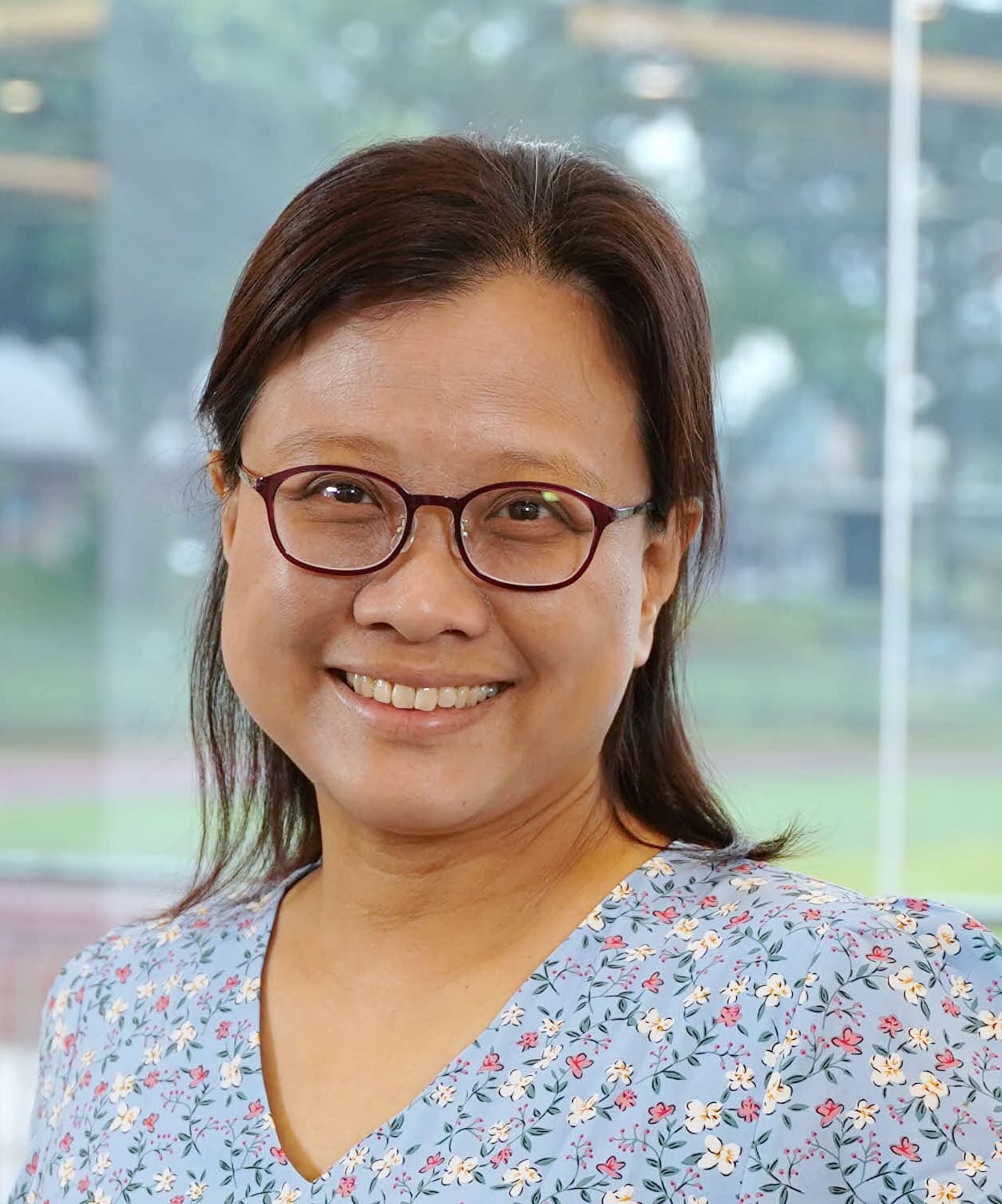 A smiling middle-aged woman with brown hair and red-framed glasses wearing a light blue floral top.