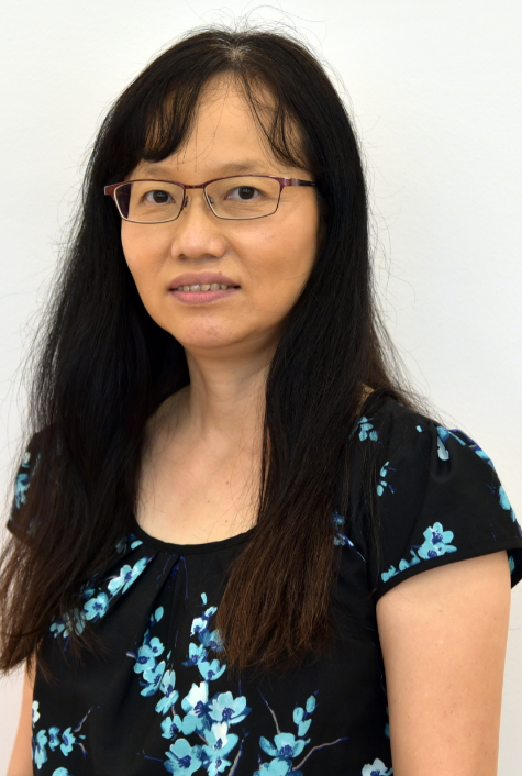 A woman with long dark hair and glasses wearing a black floral top, smiling slightly against a white background.