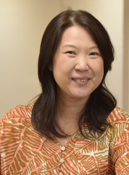 A smiling middle-aged woman with dark shoulder-length hair wearing an orange and white leaf-patterned blouse.