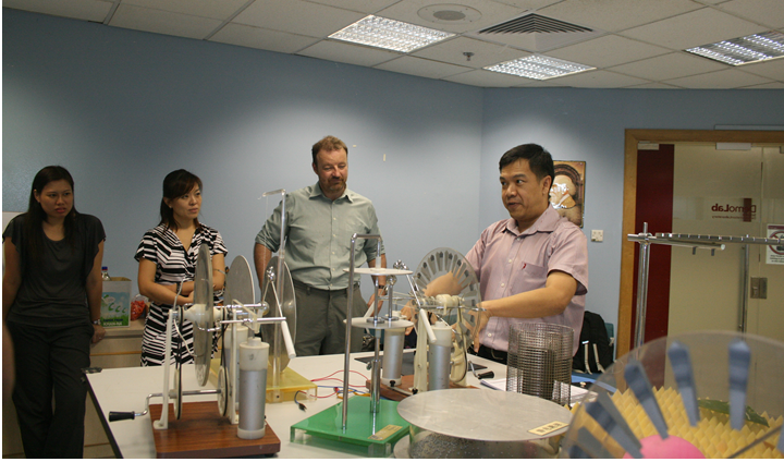 Four people stand around a table covered with mechanical models and equipment in an indoor room.