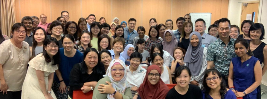 A large diverse group of smiling adults posing together indoors for a group photo.