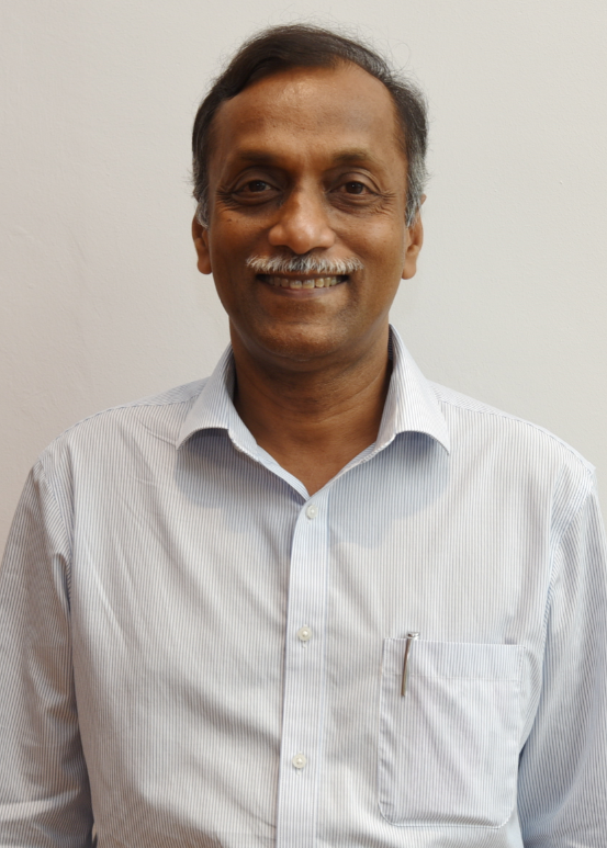 A middle-aged man with a grey mustache smiling, wearing a light blue striped shirt against a plain white background.