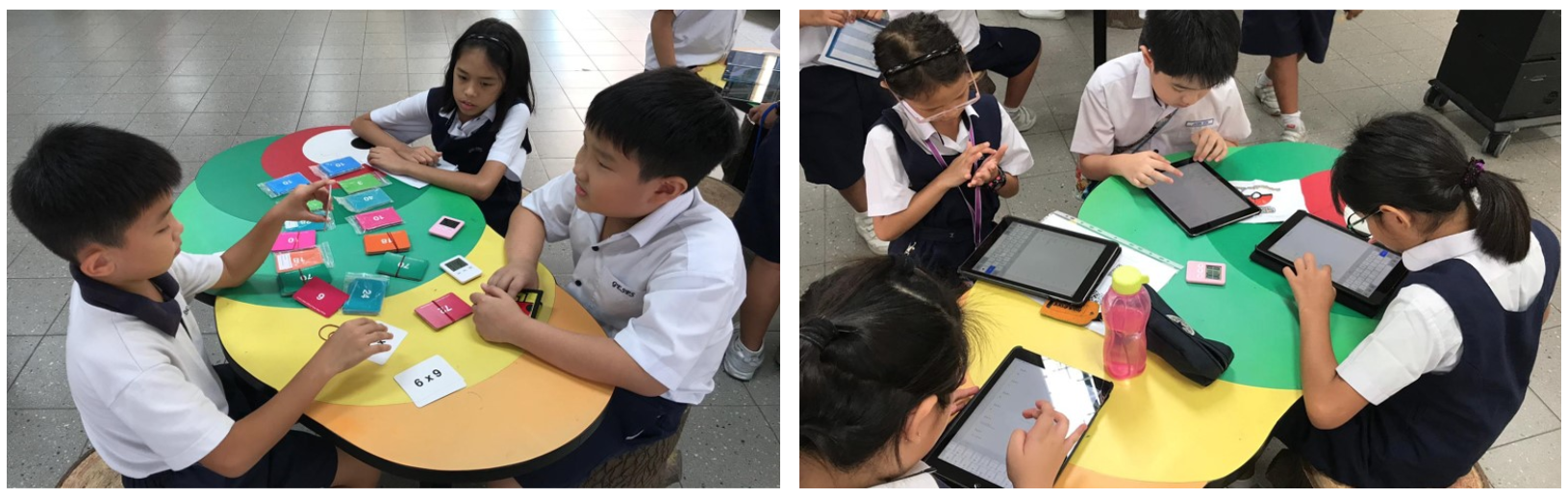 Children in uniforms sit at colorful round tables, using math cards and tablets during a group learning activity.