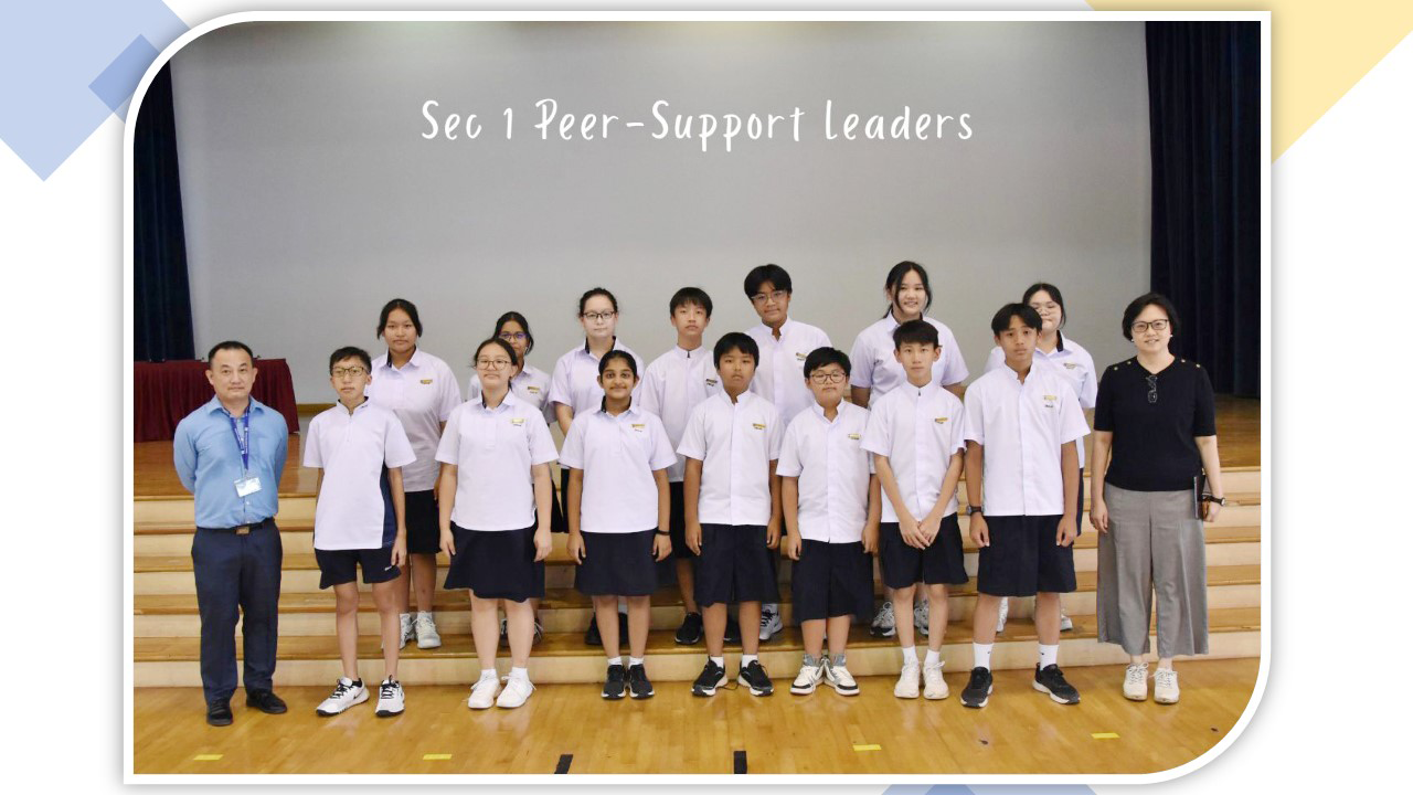 Group of Secondary 1 Peer-Support Leaders in school uniforms posing with two adults in a school hall.