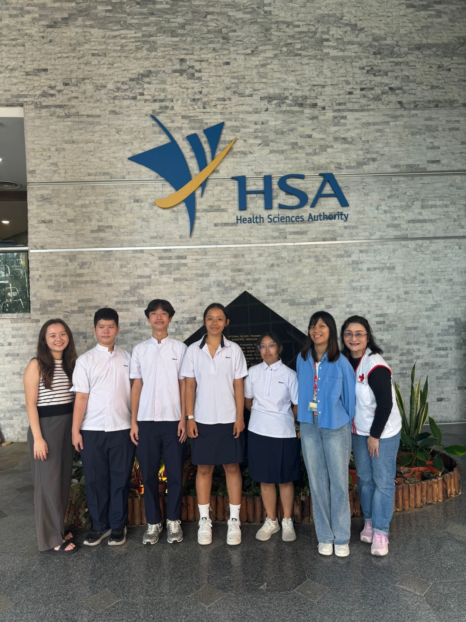 Seven people, including students and staff, pose beneath the HSA Health Sciences Authority sign outdoors.