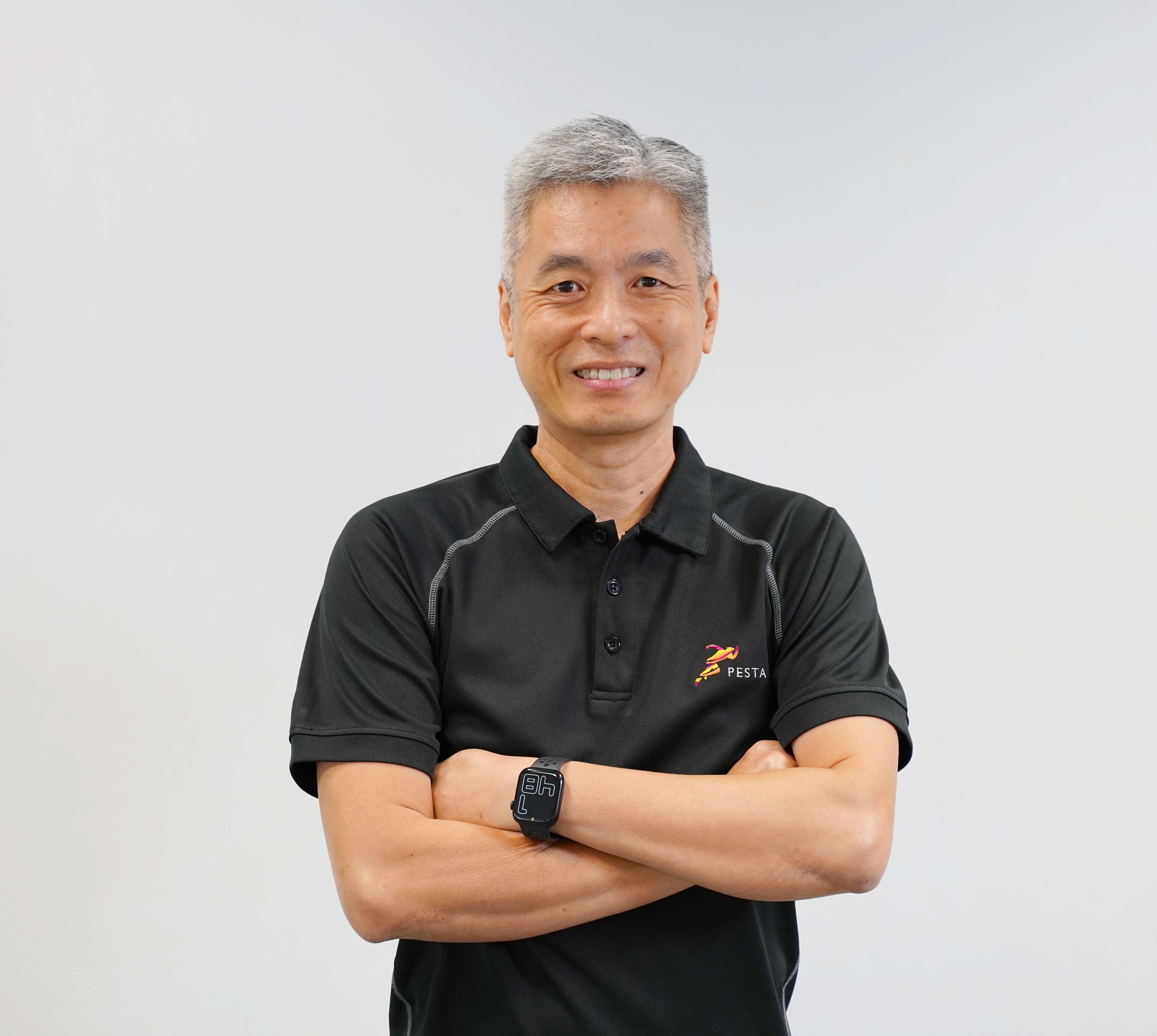 Middle-aged man with gray hair, smiling, arms crossed, wearing a black Pesta polo shirt and a smartwatch.
