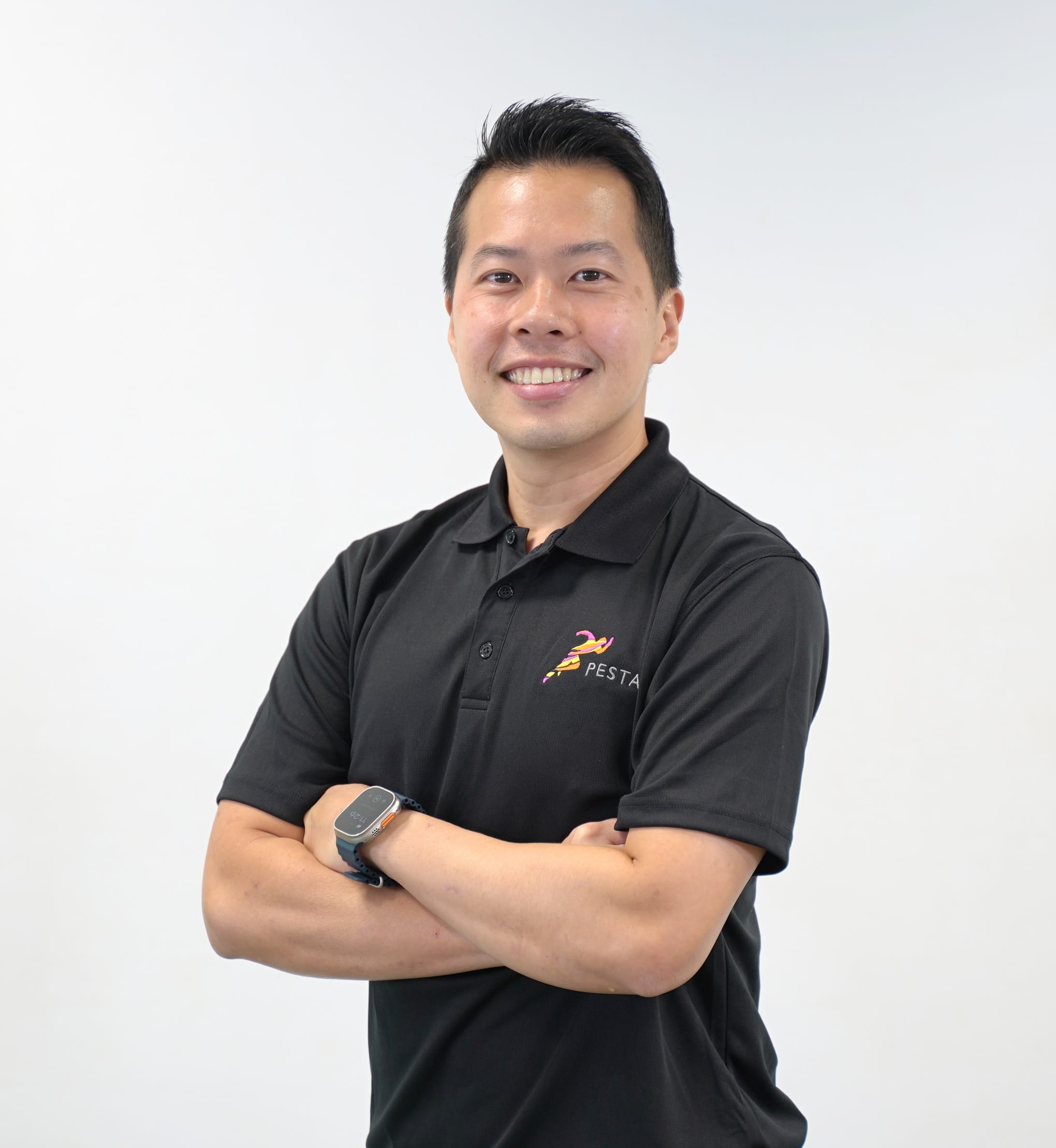 A smiling man with arms crossed wearing a black polo shirt with a Pesta logo and a smartwatch.