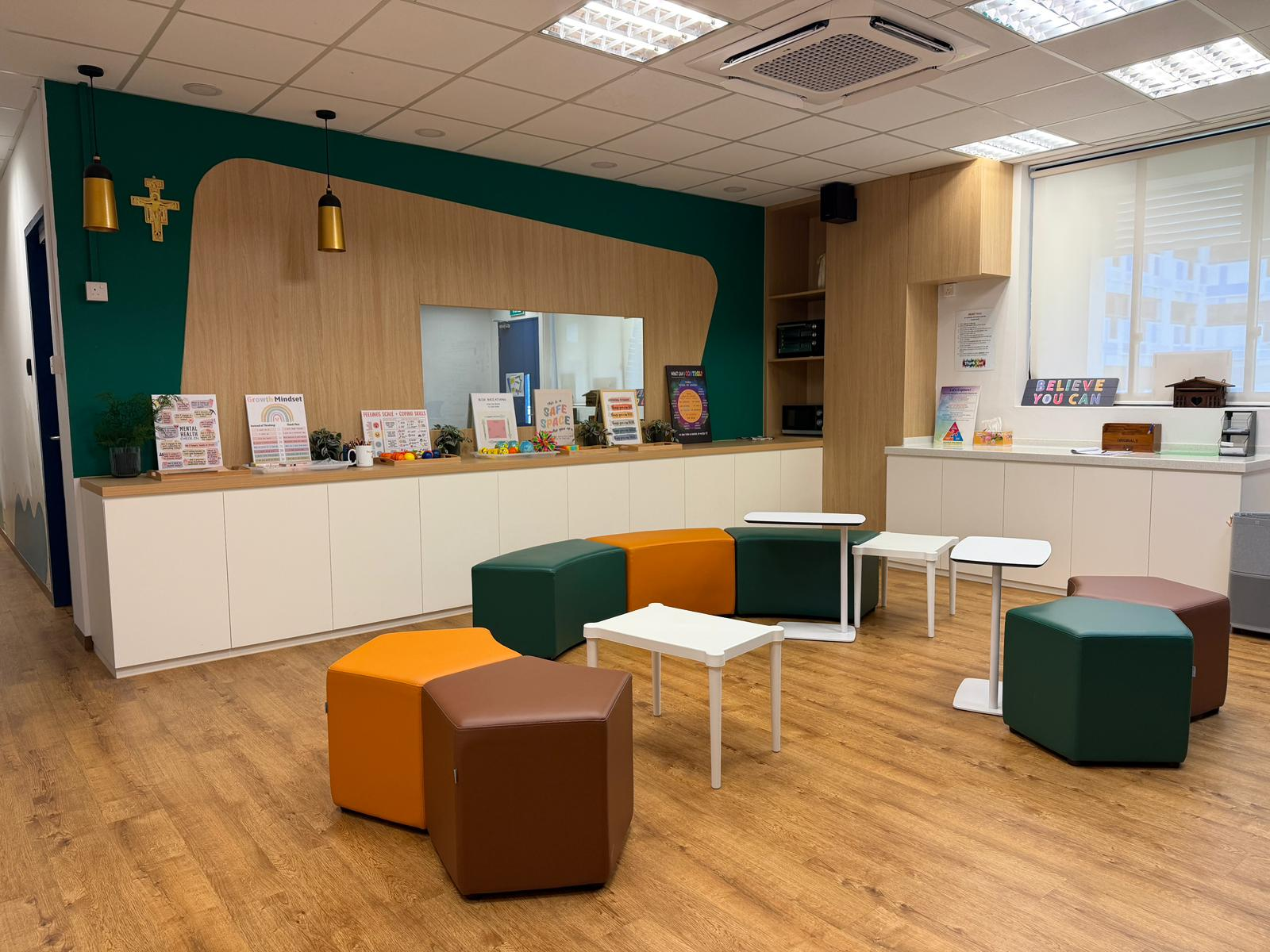 Bright counseling room with colorful hexagonal stools, white tables, teal accent wall, and motivational posters on a wood counter.