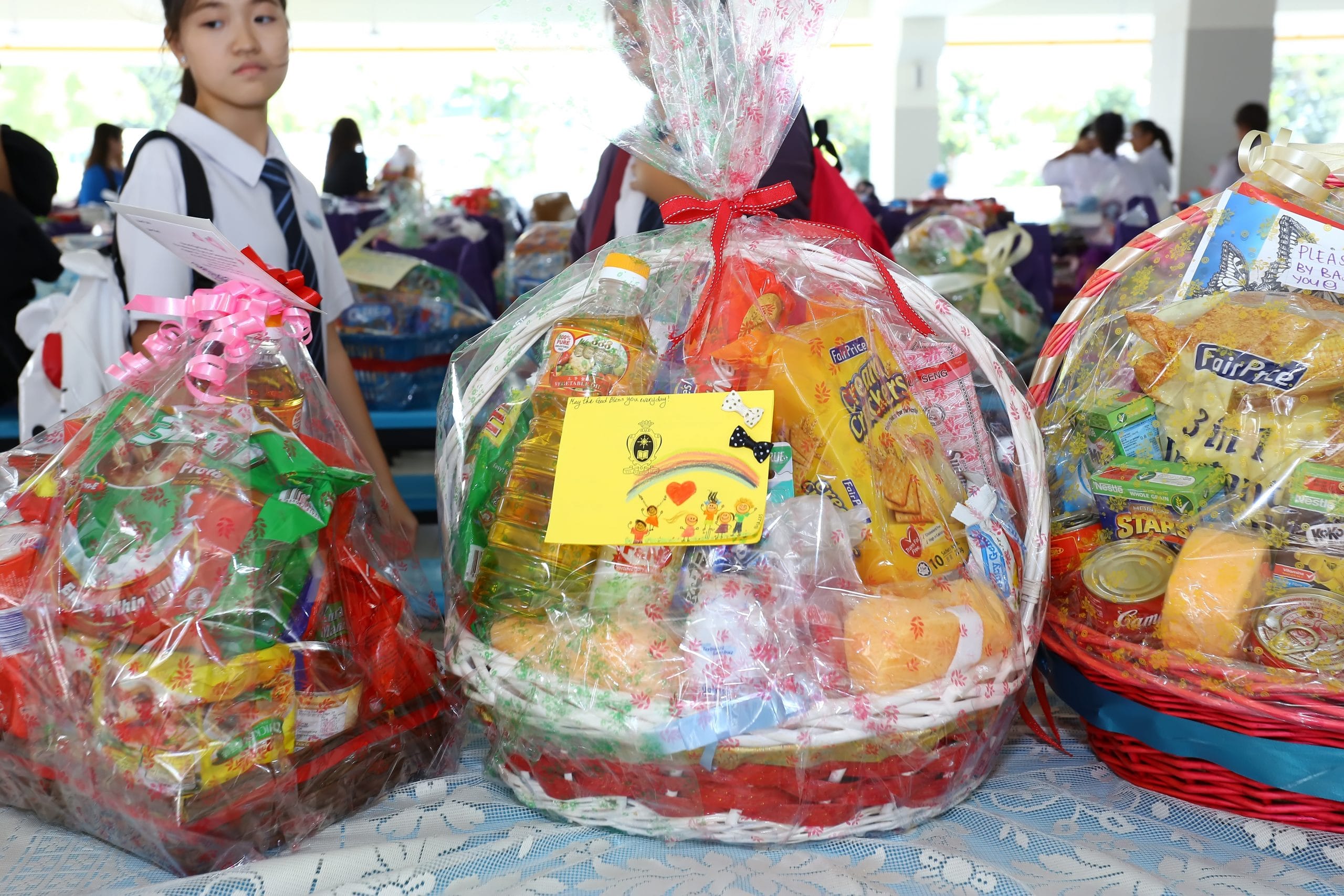 Hampers filled with groceries and household essentials, each decorated with handwritten cards, assembled by uniformed students as part of a community giving initiative.