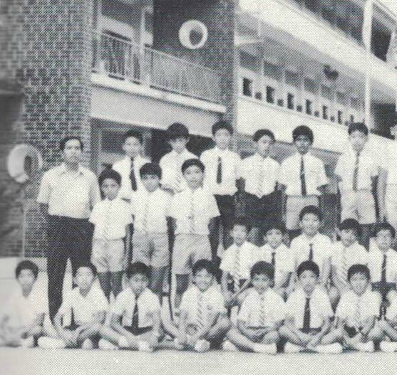 Black and white photo of a group of young male students in uniforms posing with an adult in front of a school building.