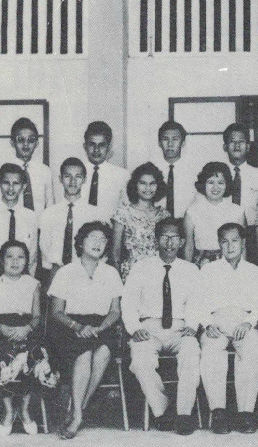 Black and white group photo of about 12 people posed in three rows, men in ties and women in light blouses.