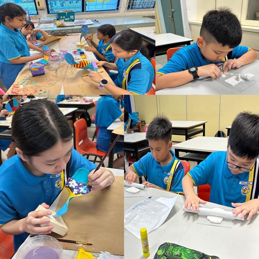 Four children in blue uniforms work on art and craft projects at classroom desks, painting and assembling models.