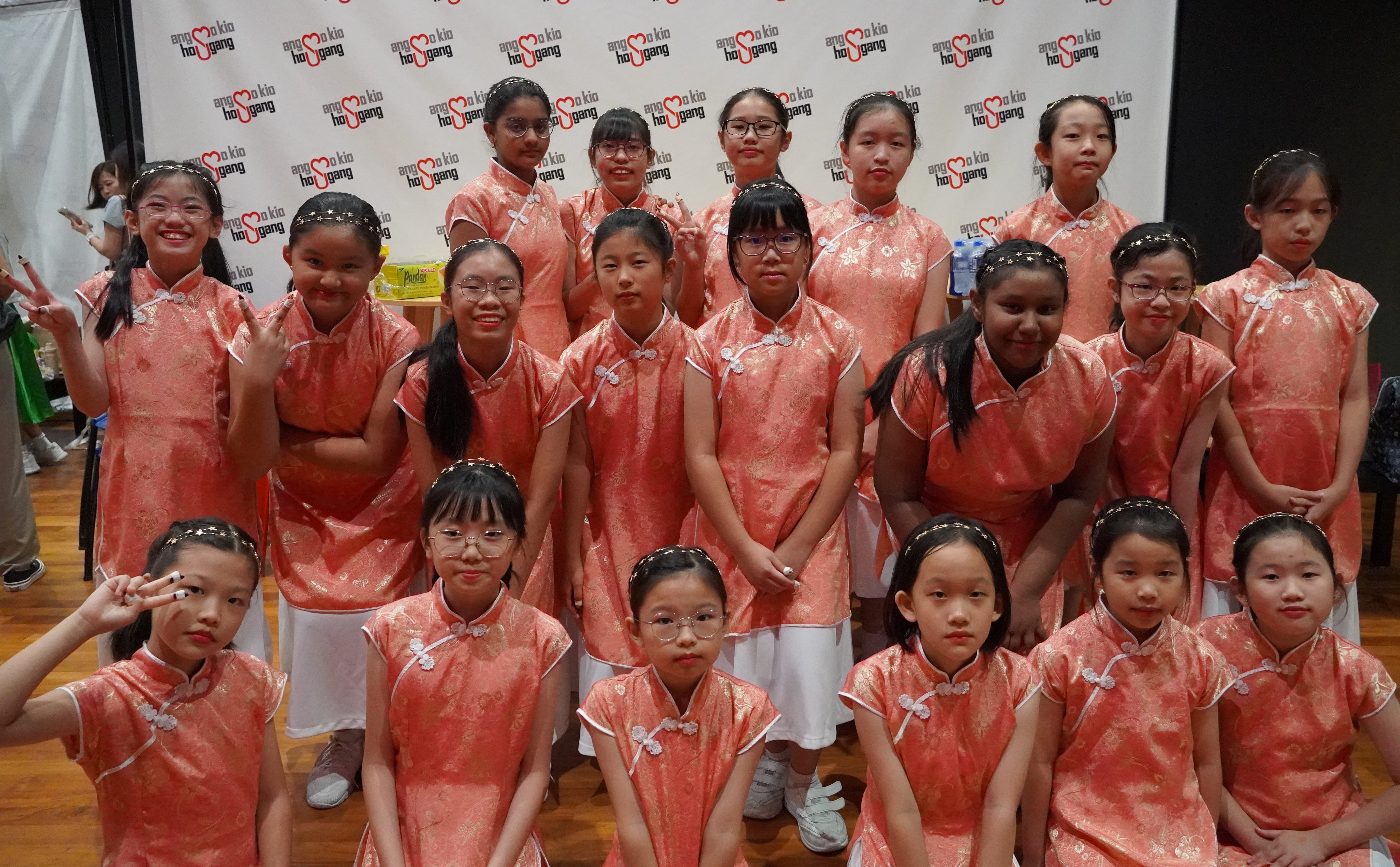 Group of girls in matching red cheongsam-style dresses posing in front of a patterned backdrop.