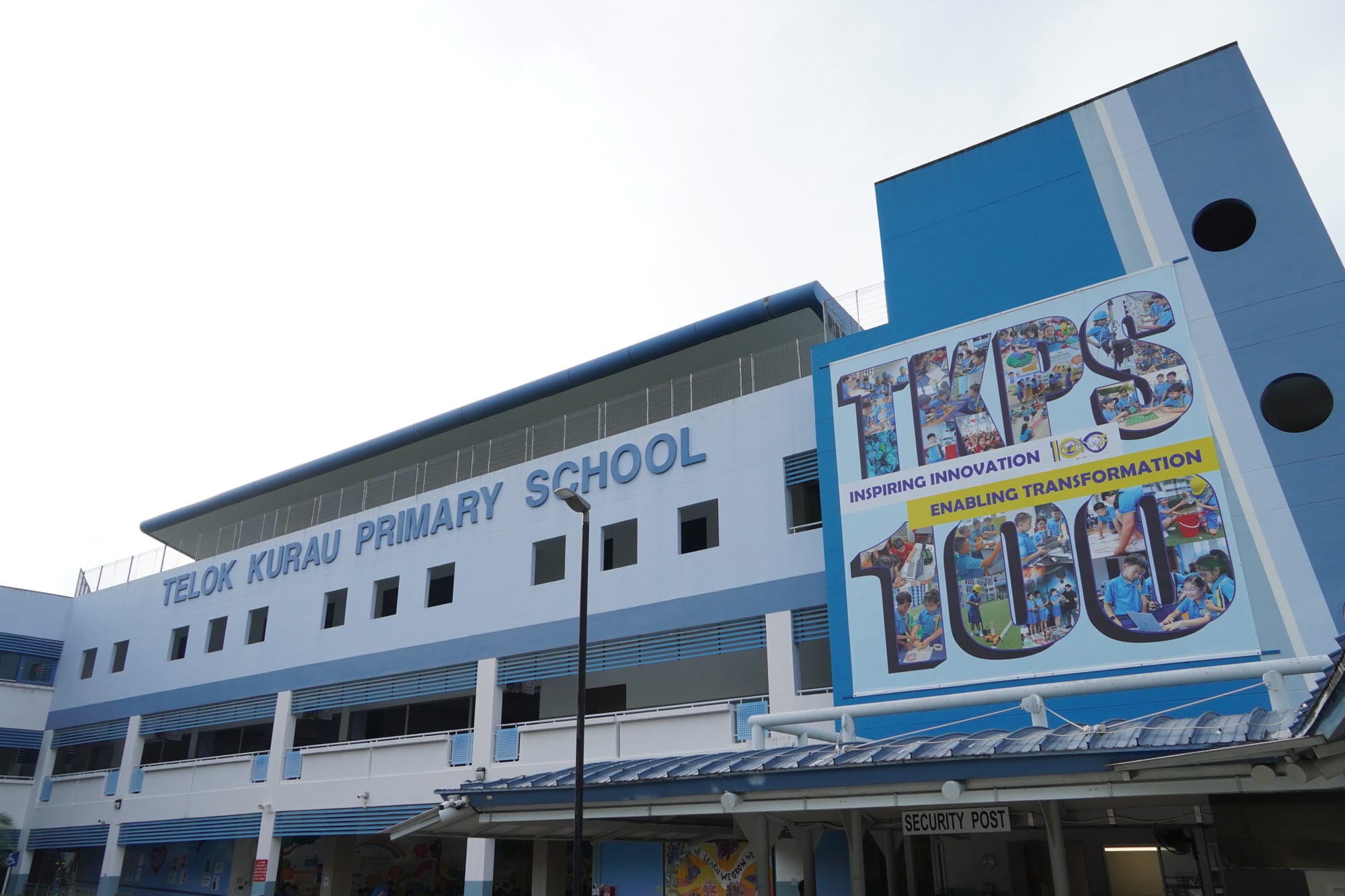 Telok Kurau Primary School building in blue and white with a TKPS 100th anniversary banner on the facade.