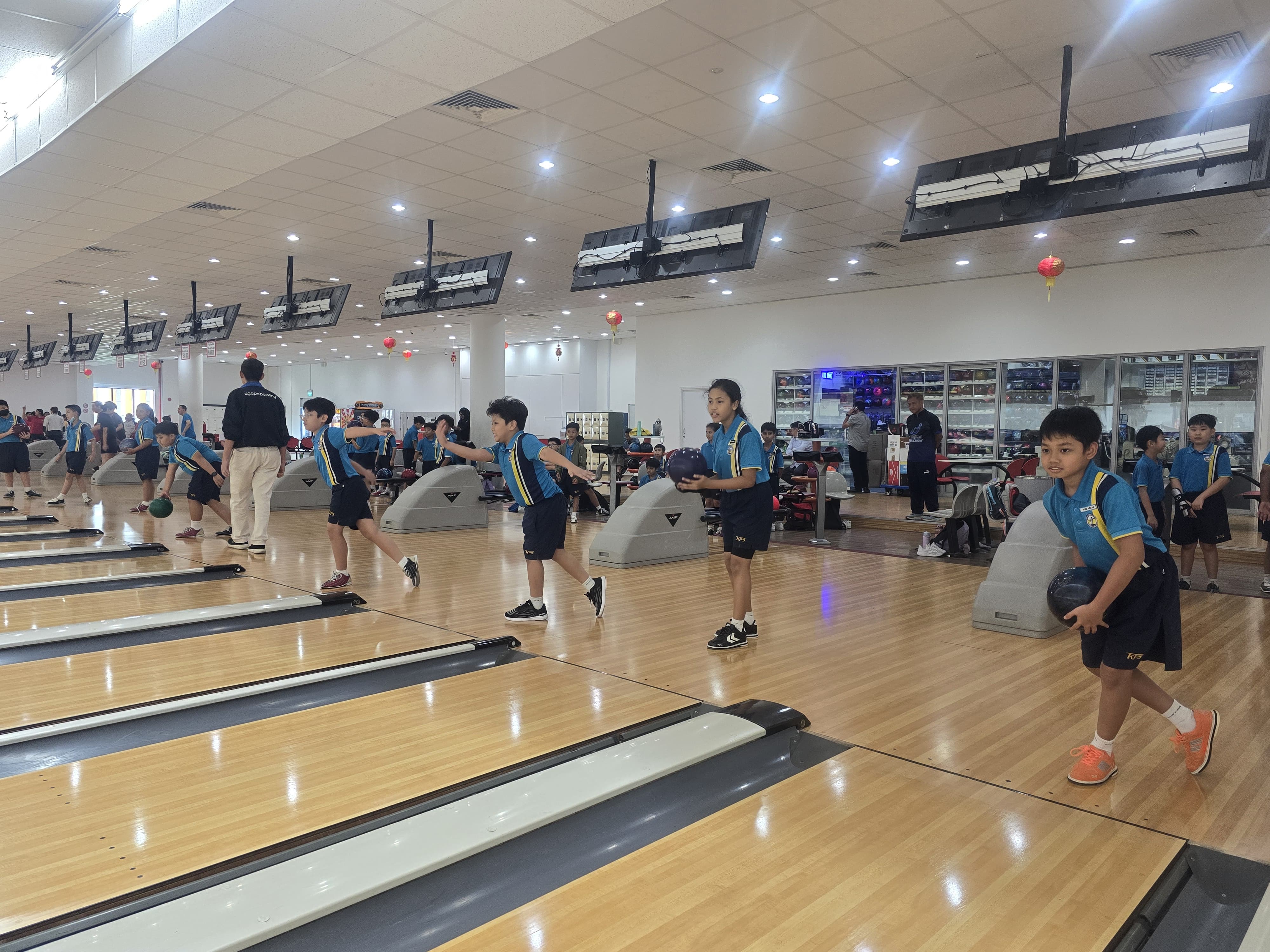 Children in matching blue uniforms bowling on multiple lanes in a large indoor bowling alley.