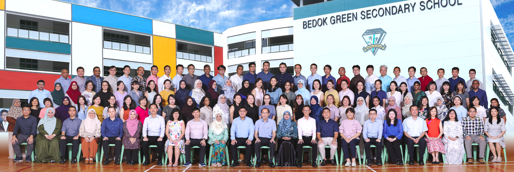 Large group of staff posing in front of Bedok Green Secondary School building with colorful facade.