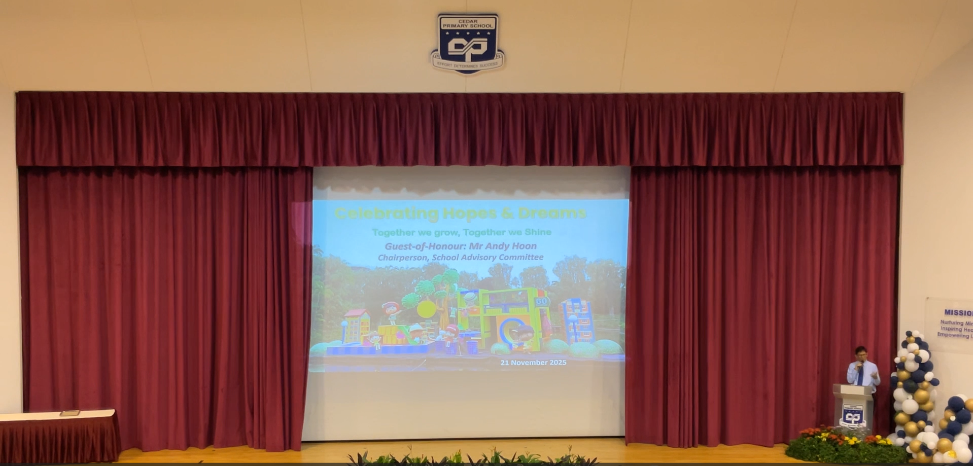 Cedar Primary School hall with a projected slide reading "Celebrating Hopes and Dreams" dated 21 November 2025.