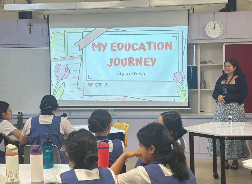 A woman presents a slide titled "My Education Journey by Annika" to students in school uniforms in a classroom.