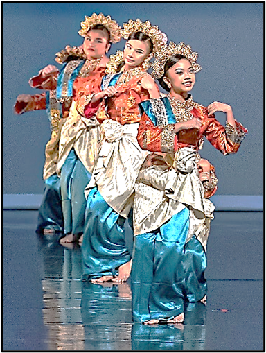 Three young female dancers in traditional Indonesian dance costumes with gold headdresses perform on a stage.
