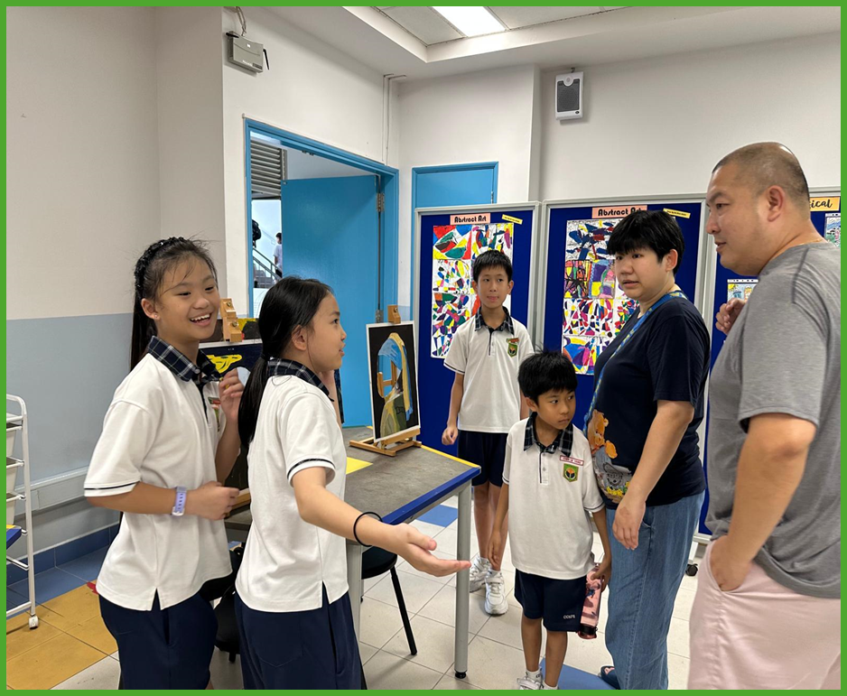 Students in white uniforms present artwork to two adults in a classroom with colorful abstract art displayed on boards.