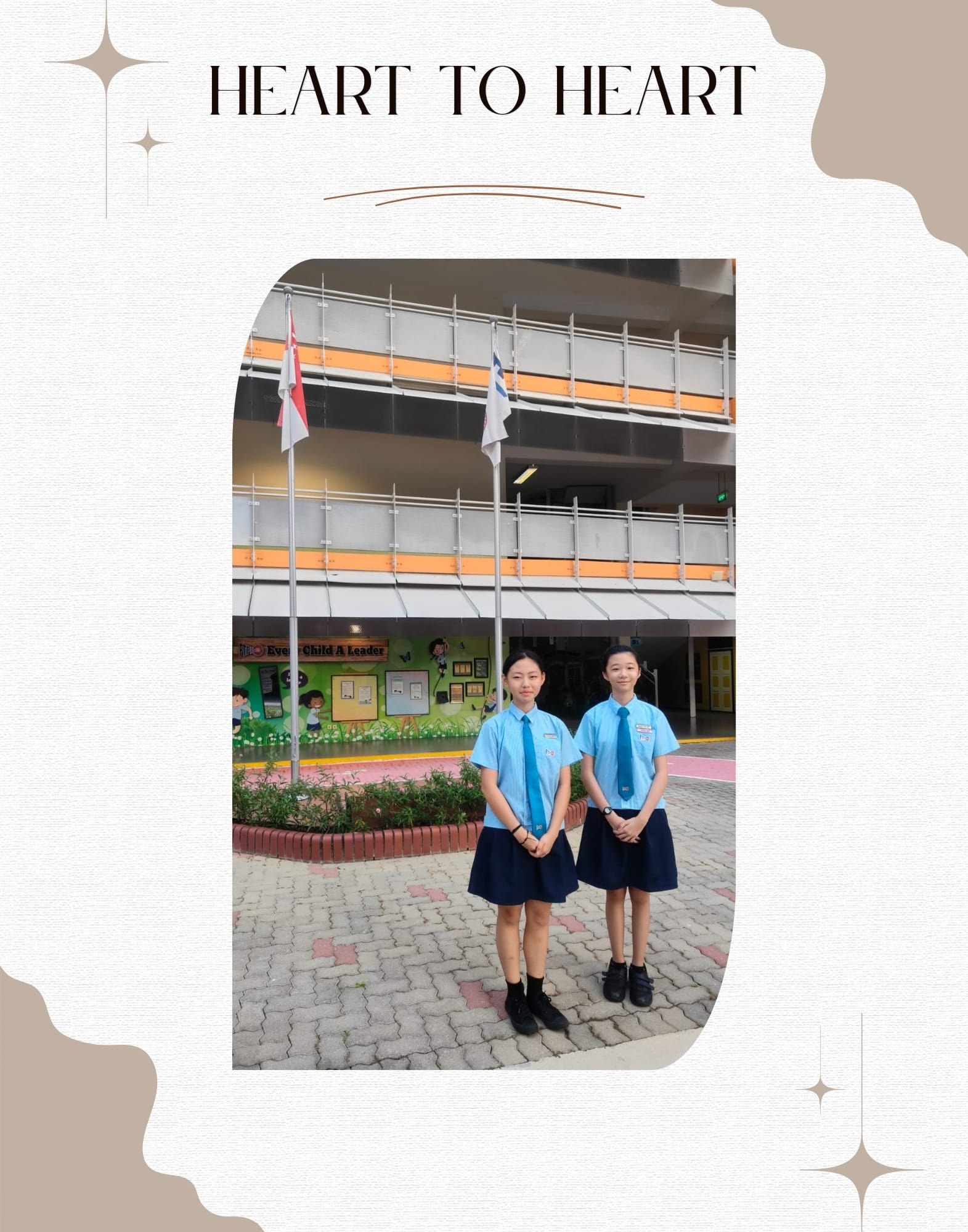 Two girls in blue school uniforms and navy skirts stand in a school courtyard with flagpoles and a mural behind them.