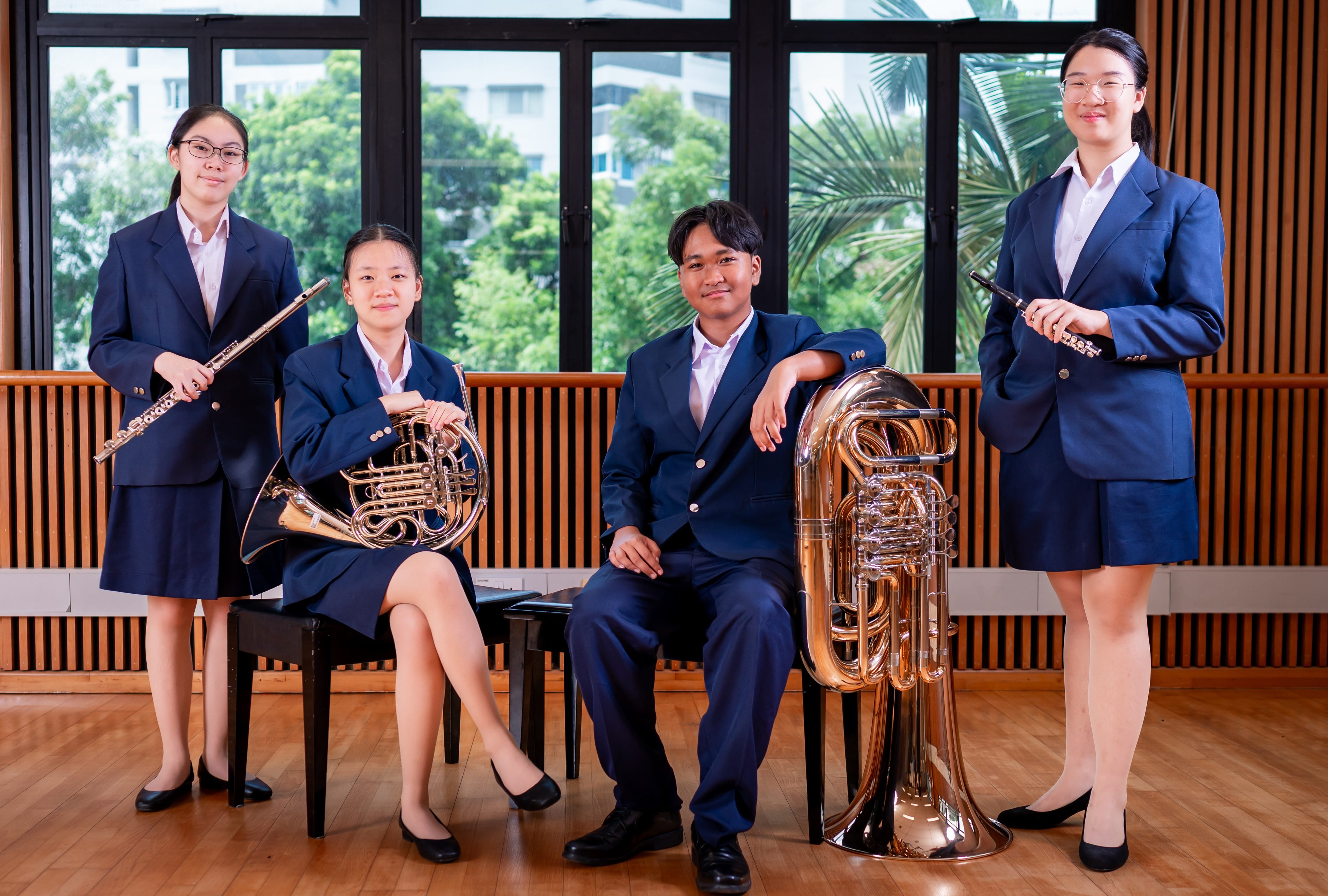Four students in navy uniforms pose with instruments: two flutes, a French horn, and a tuba.