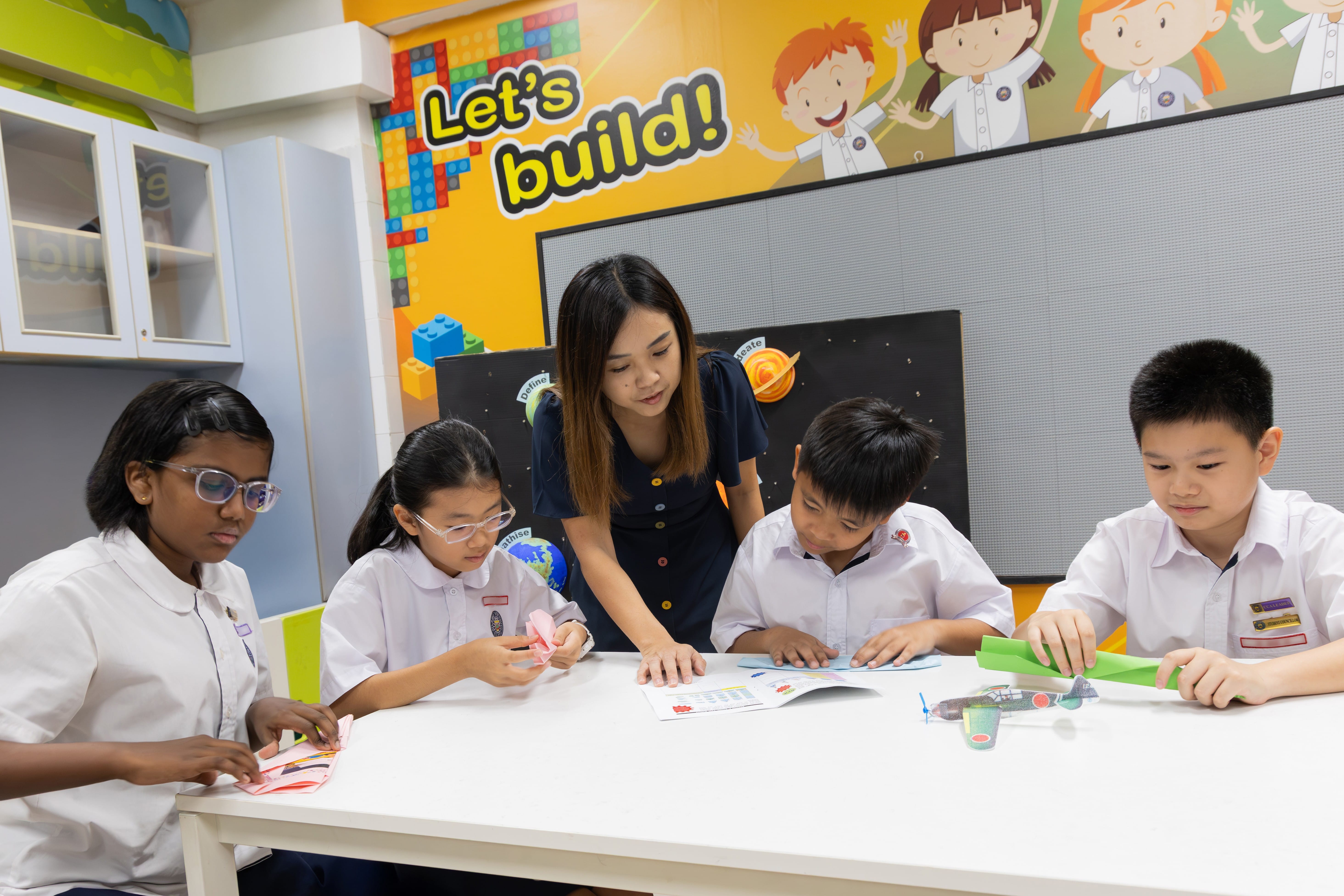 A teacher guides pupils in designing and making paper aeroplanes while applying the principles of physics.
