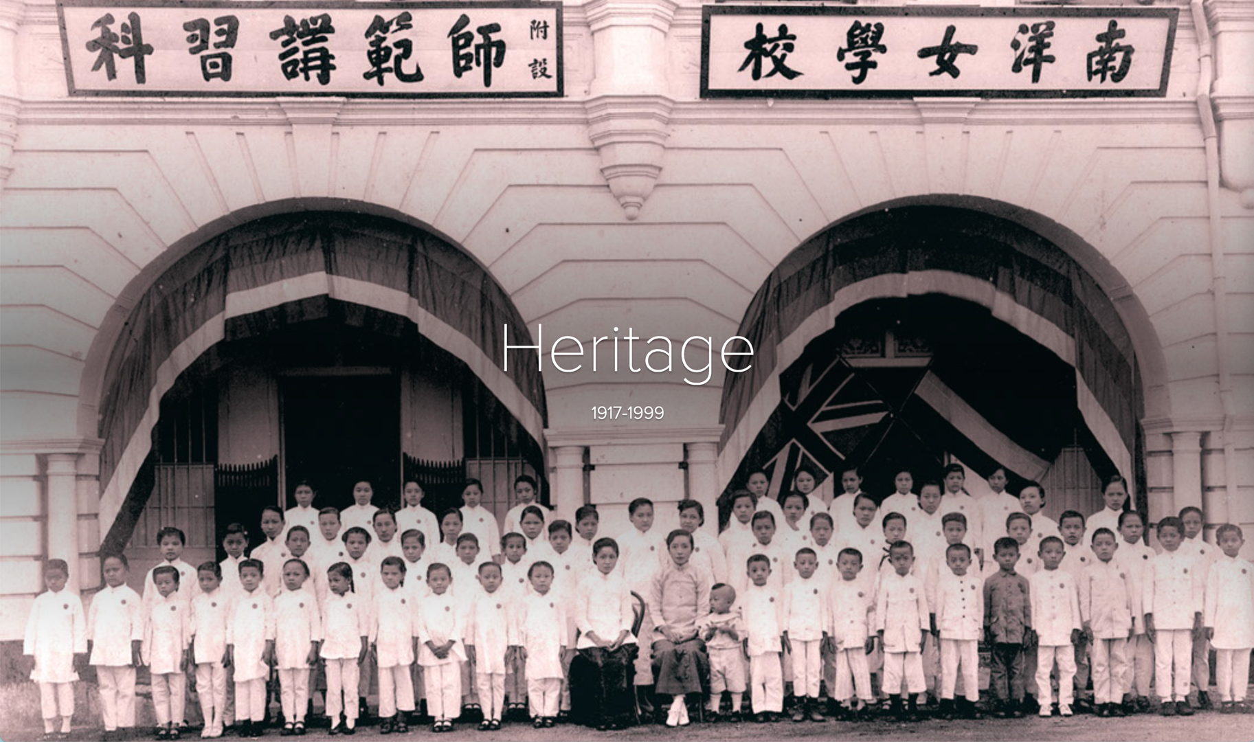 Old black and white photo of uniformed children posed before a building with Chinese signs, labeled Heritage 1917-1999.