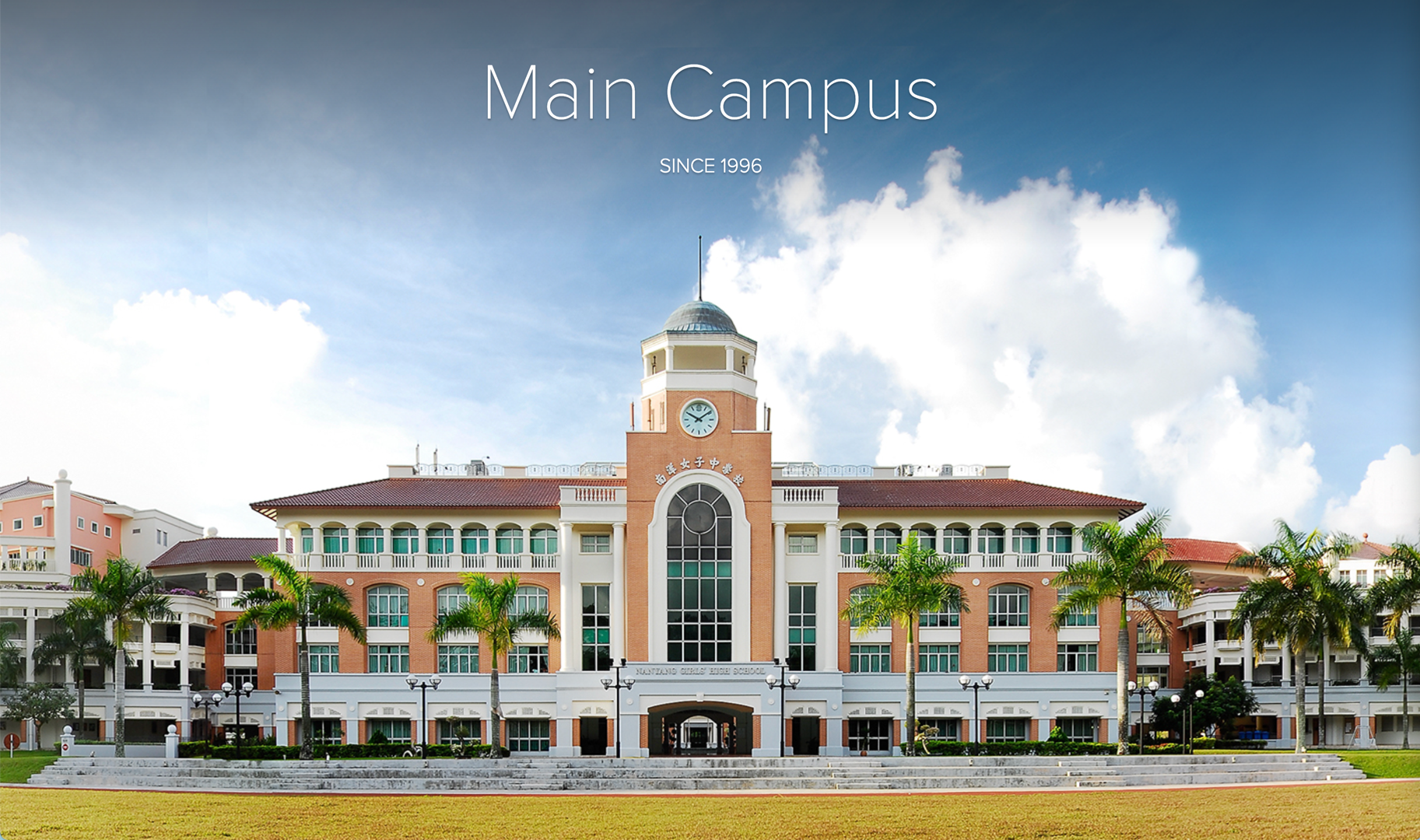 Large school building with a central clock tower, surrounded by palm trees, under a blue sky, labeled Main Campus Since 1996.