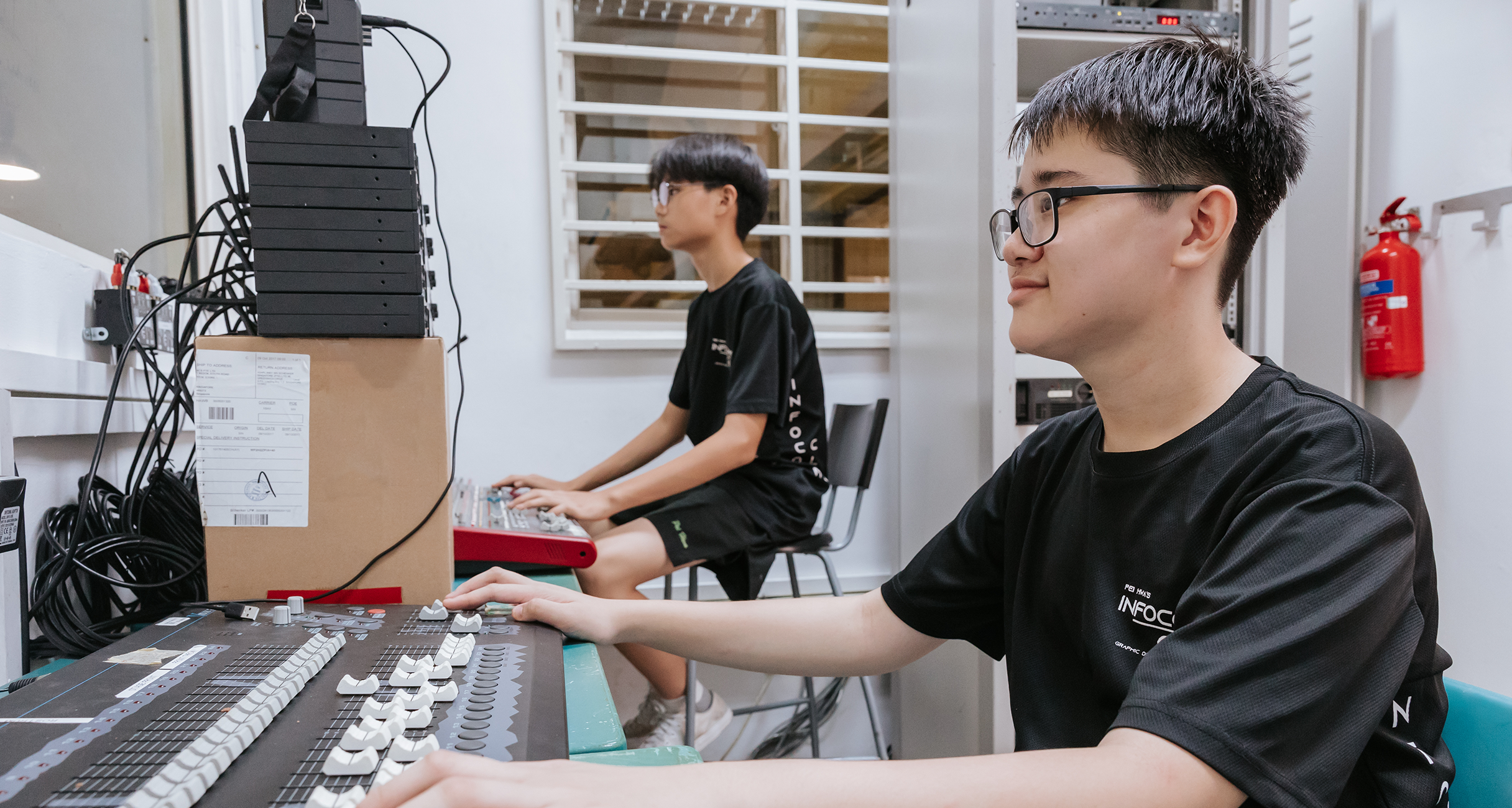 Two teens at control panels in a server room