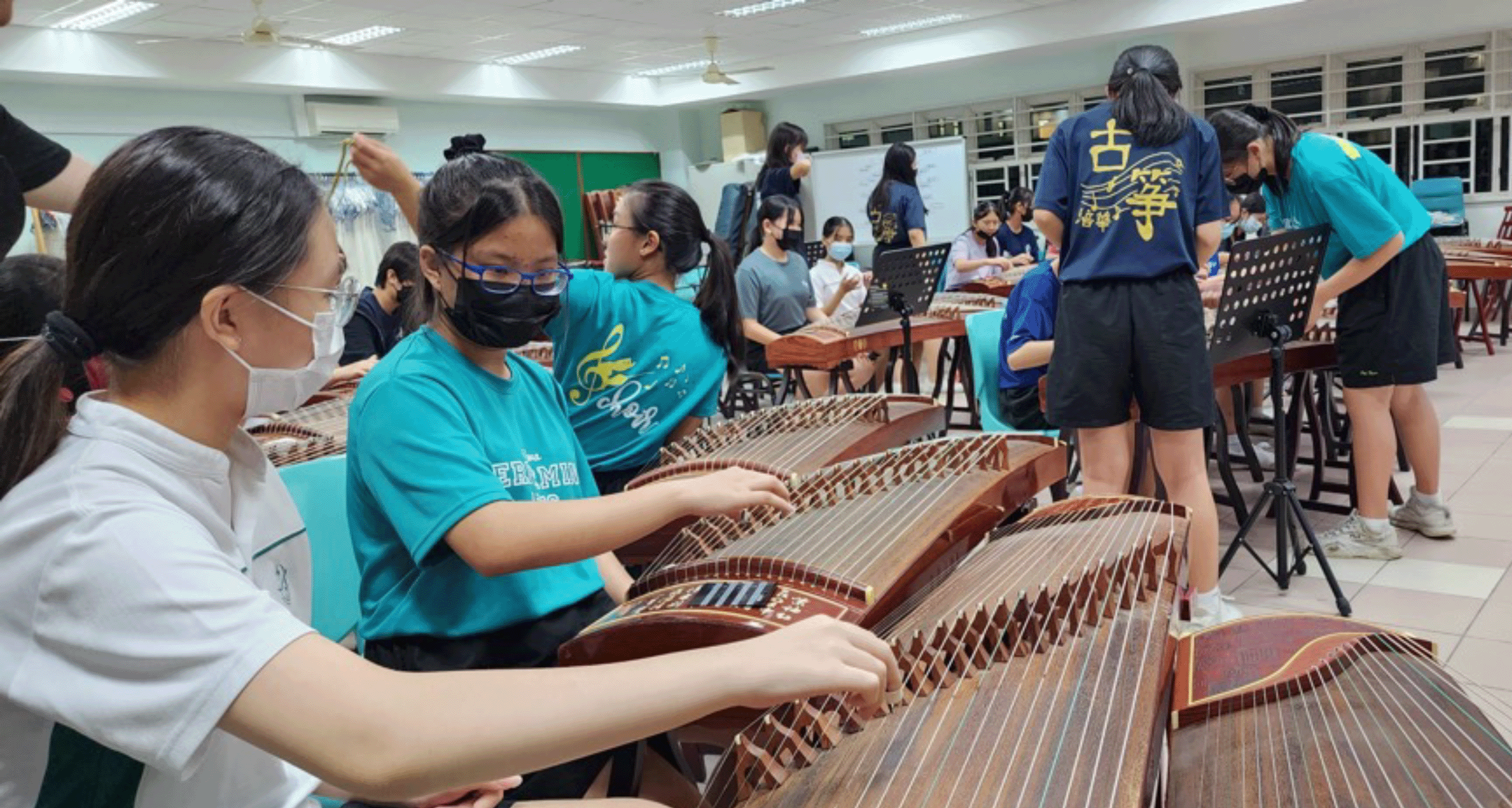 Students wearing masks practice playing guzheng instruments in a classroom setting.