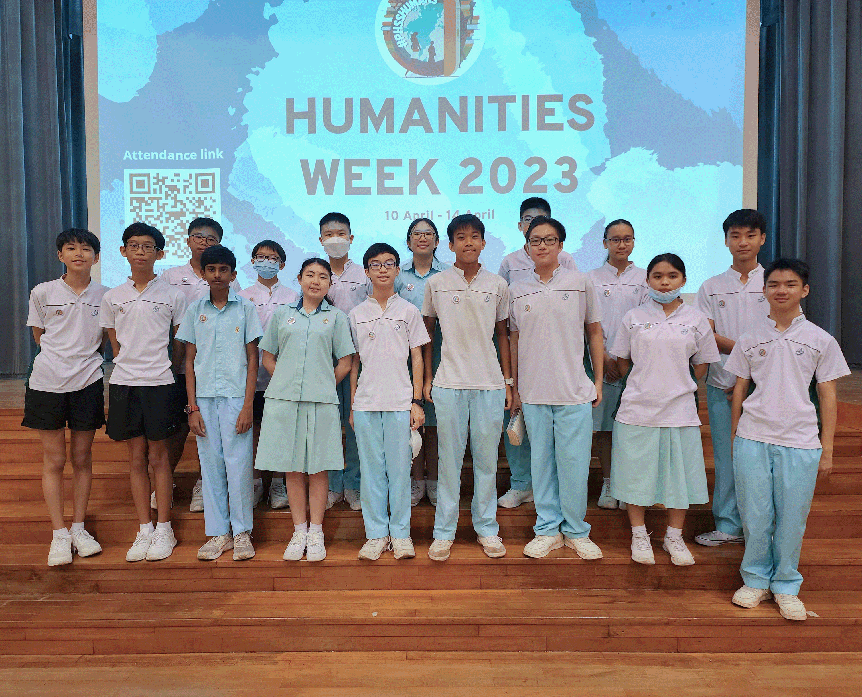 Students in uniforms stand on stage before a screen reading HUMANITIES WEEK 2023, with a QR code at left.