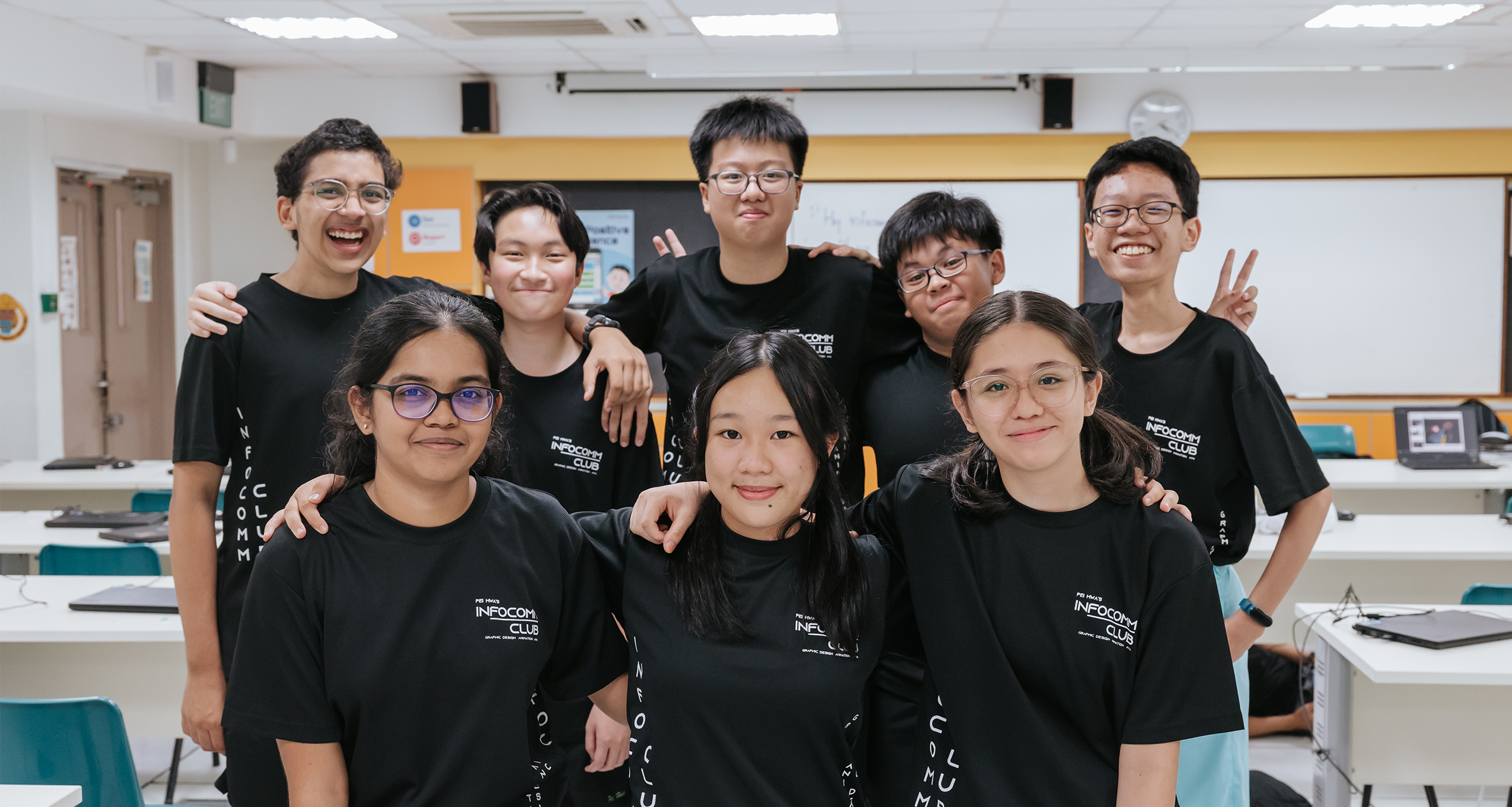 Students wearing matching black shirts pose for a photo, smiling in a classroom