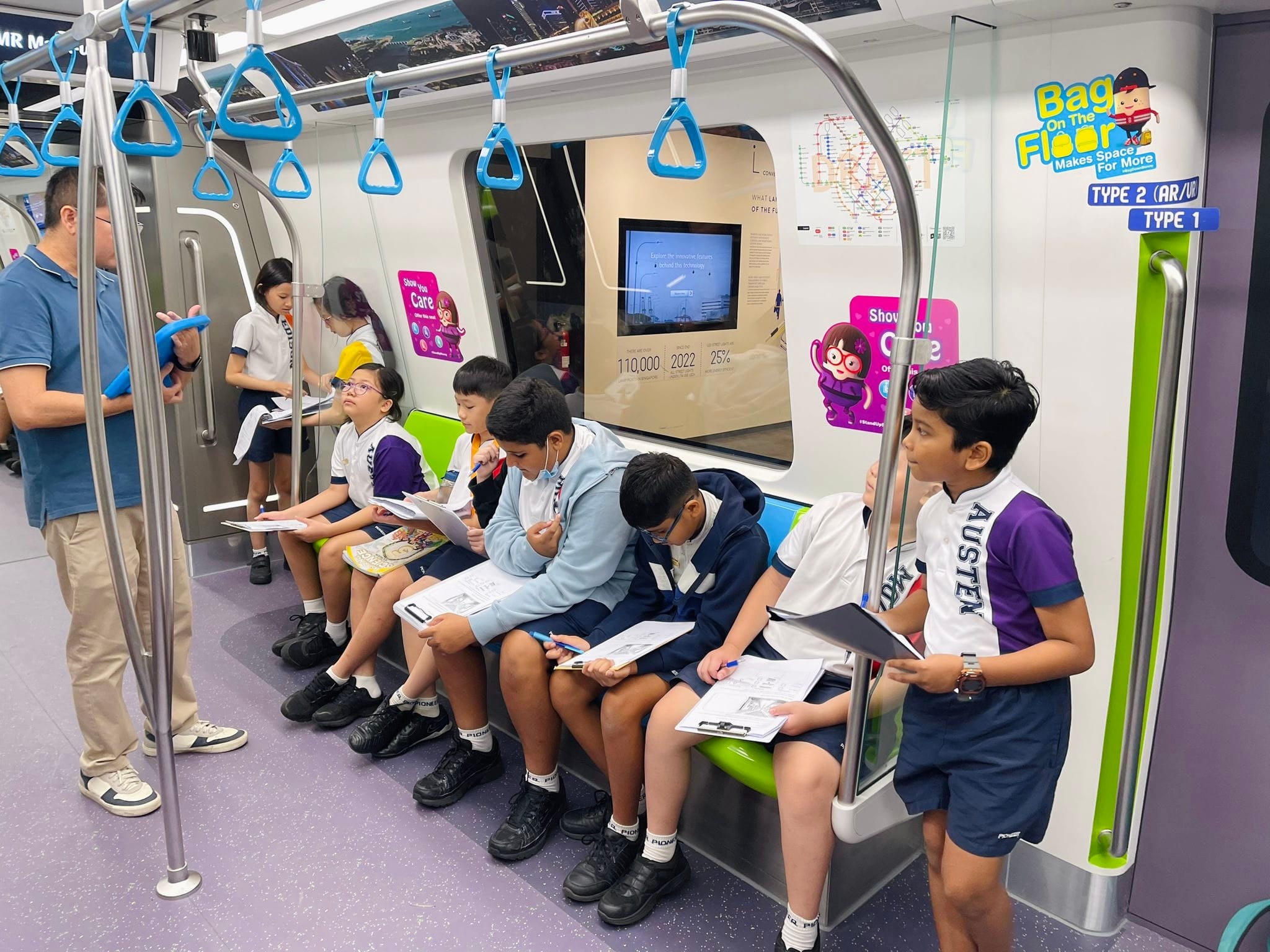 School children in uniforms sit inside a Singapore MRT train, writing on worksheets during a field trip.