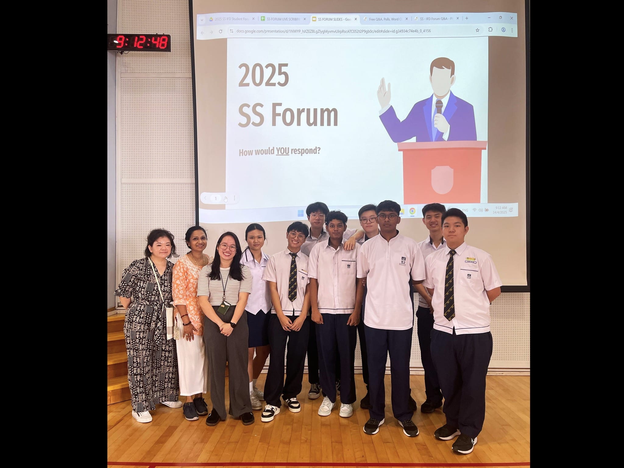 A group of students and teachers pose in front of a projected slide reading 2025 SS Forum How would YOU respond.