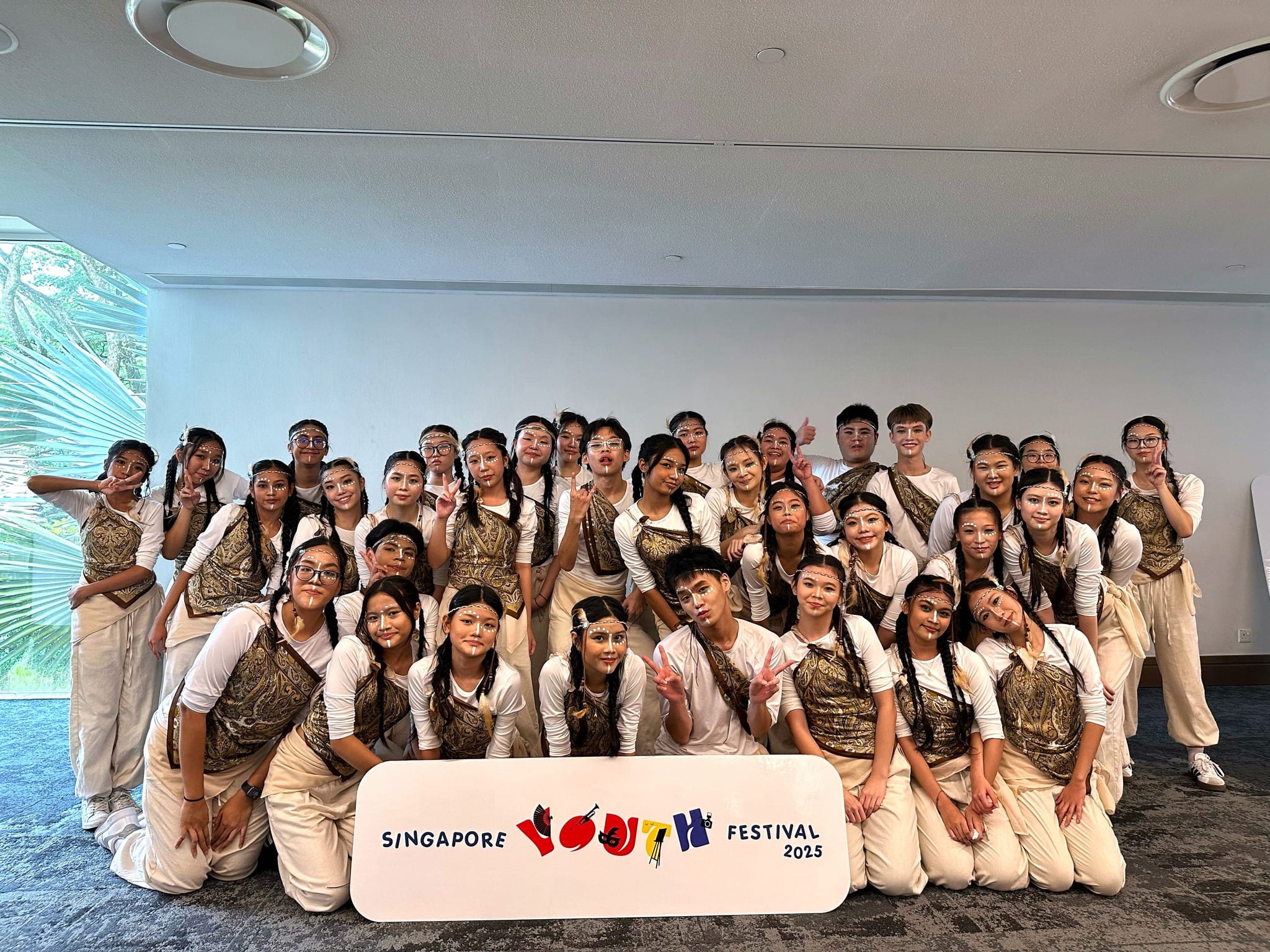 Group of young performers in white and gold costumes with face paint posing at Singapore Youth Festival 2025.
