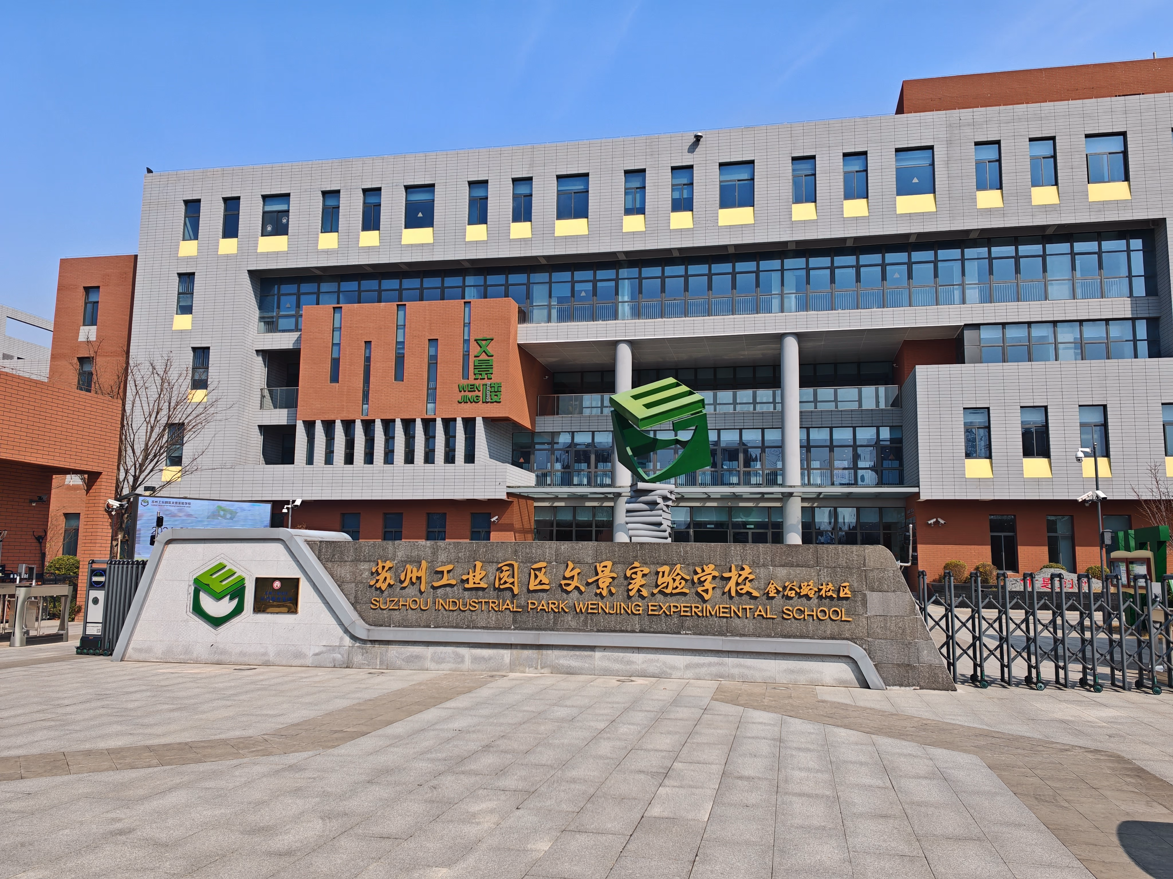 Entrance of Suzhou Industrial Park Wenjing Experimental School with a sign, green sculpture, and multi-story building.