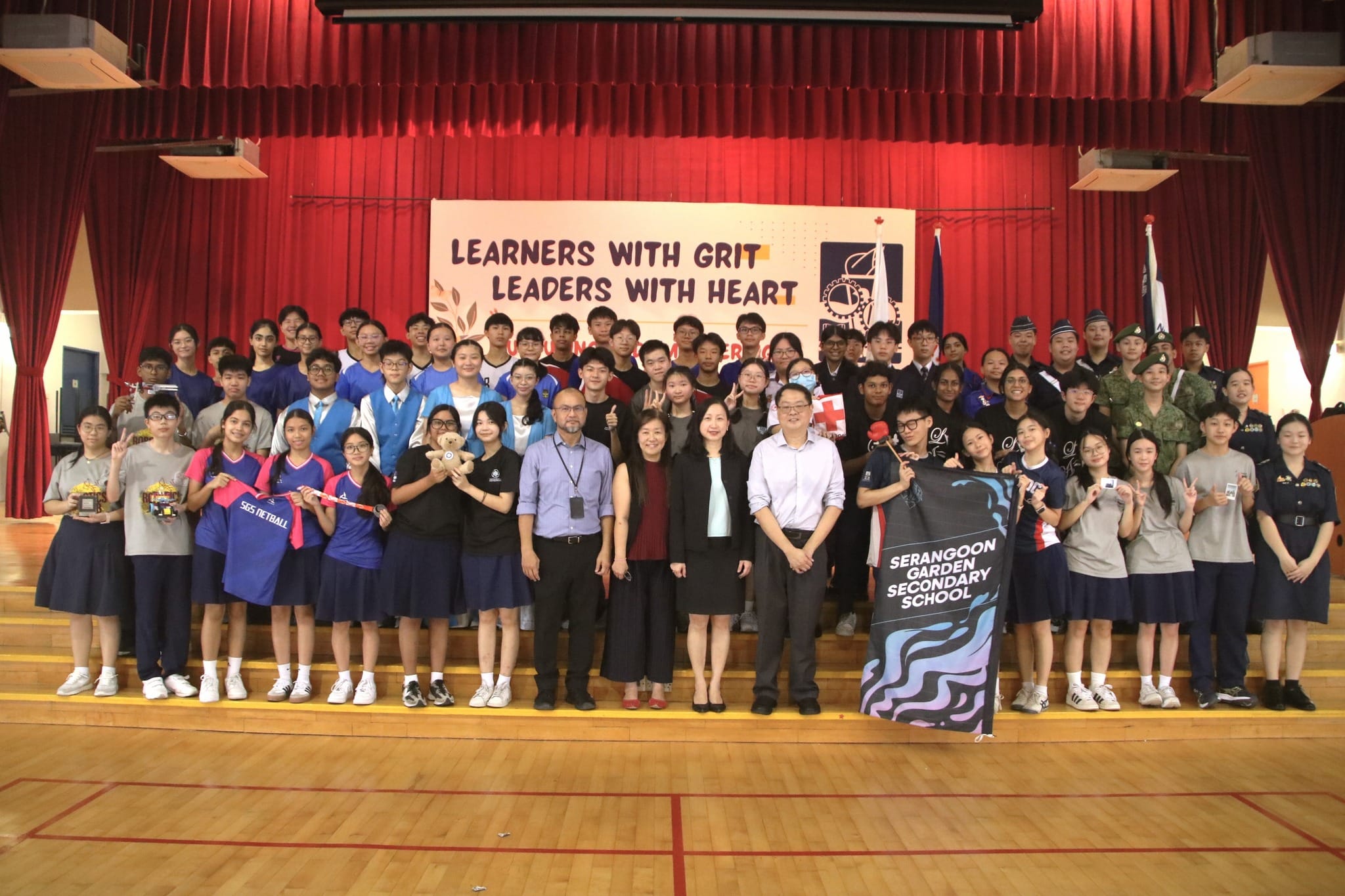 Large group of students and teachers pose at Serangoon Garden Secondary School under a banner reading Learners With Grit Leaders With Heart.