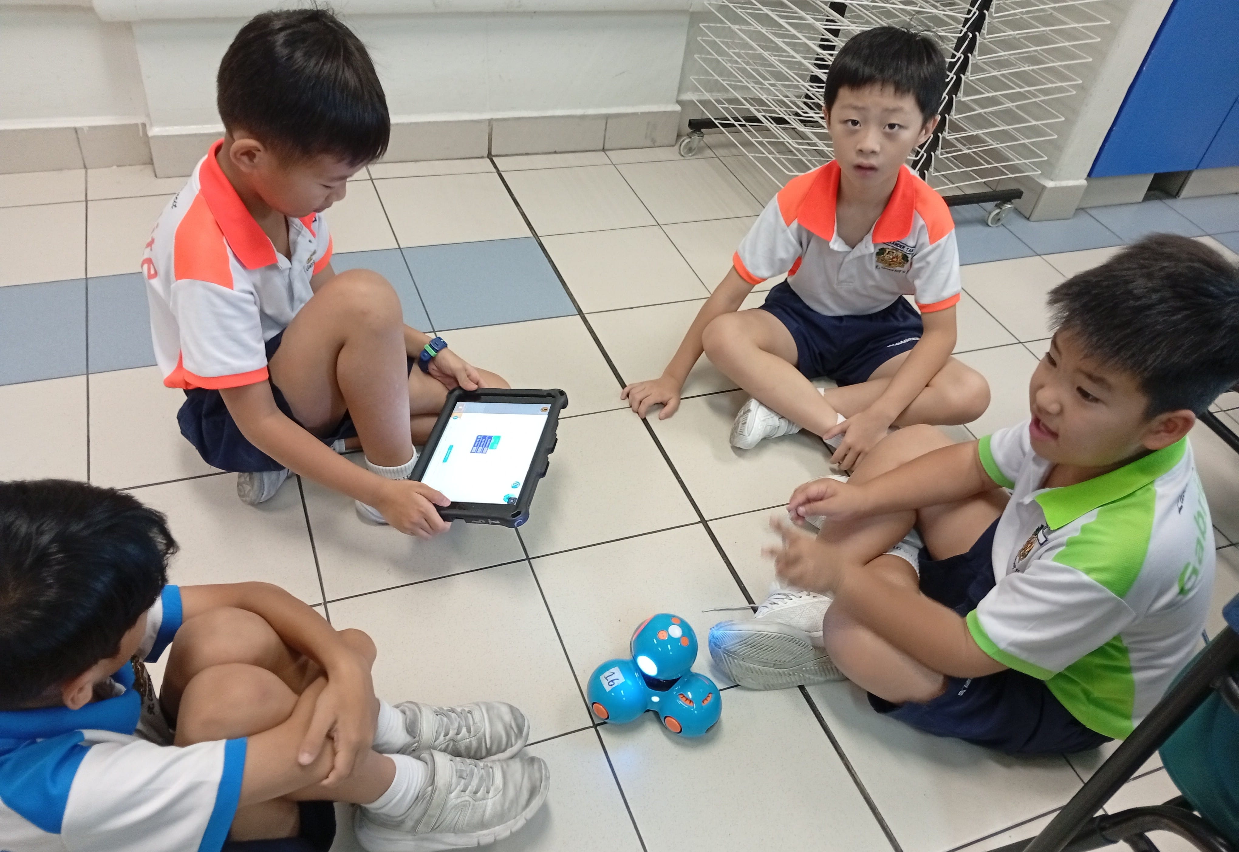 Four students sitting on the floor working on a robot with an ipad