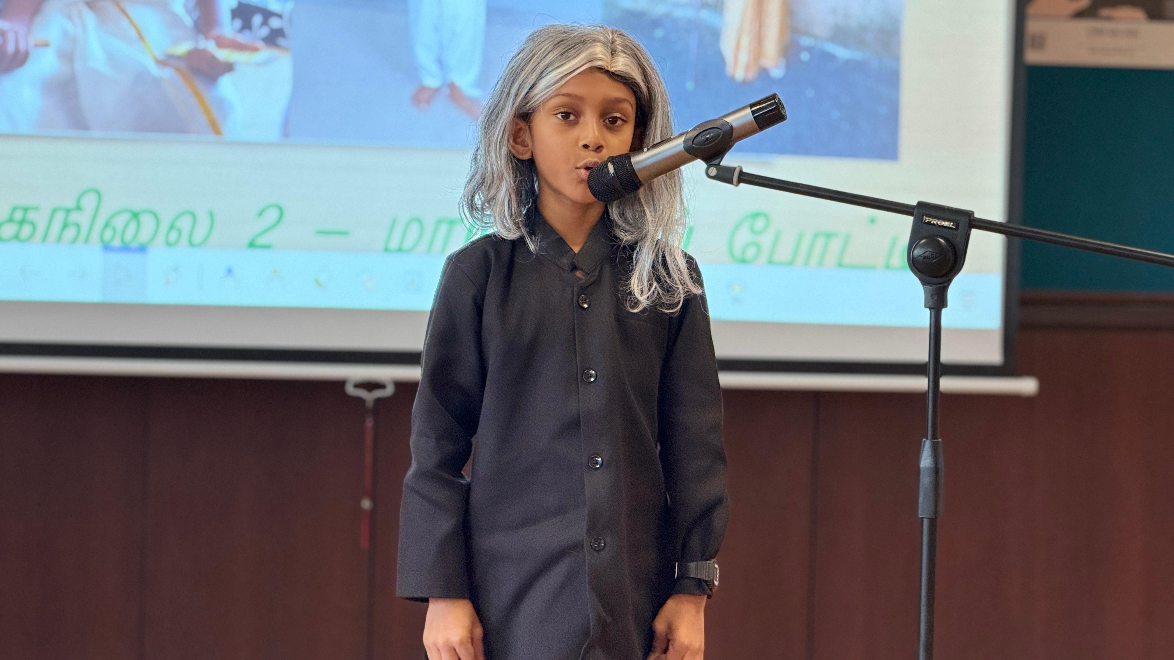 A student wearing a grey wig and black shirt portraying a character