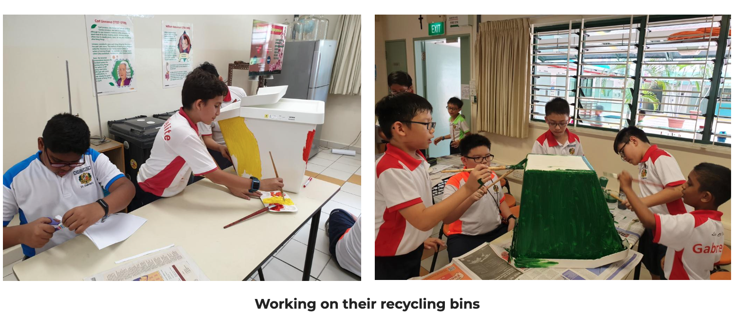 Students in red and white uniforms paint recycling bins yellow and green during a classroom activity.