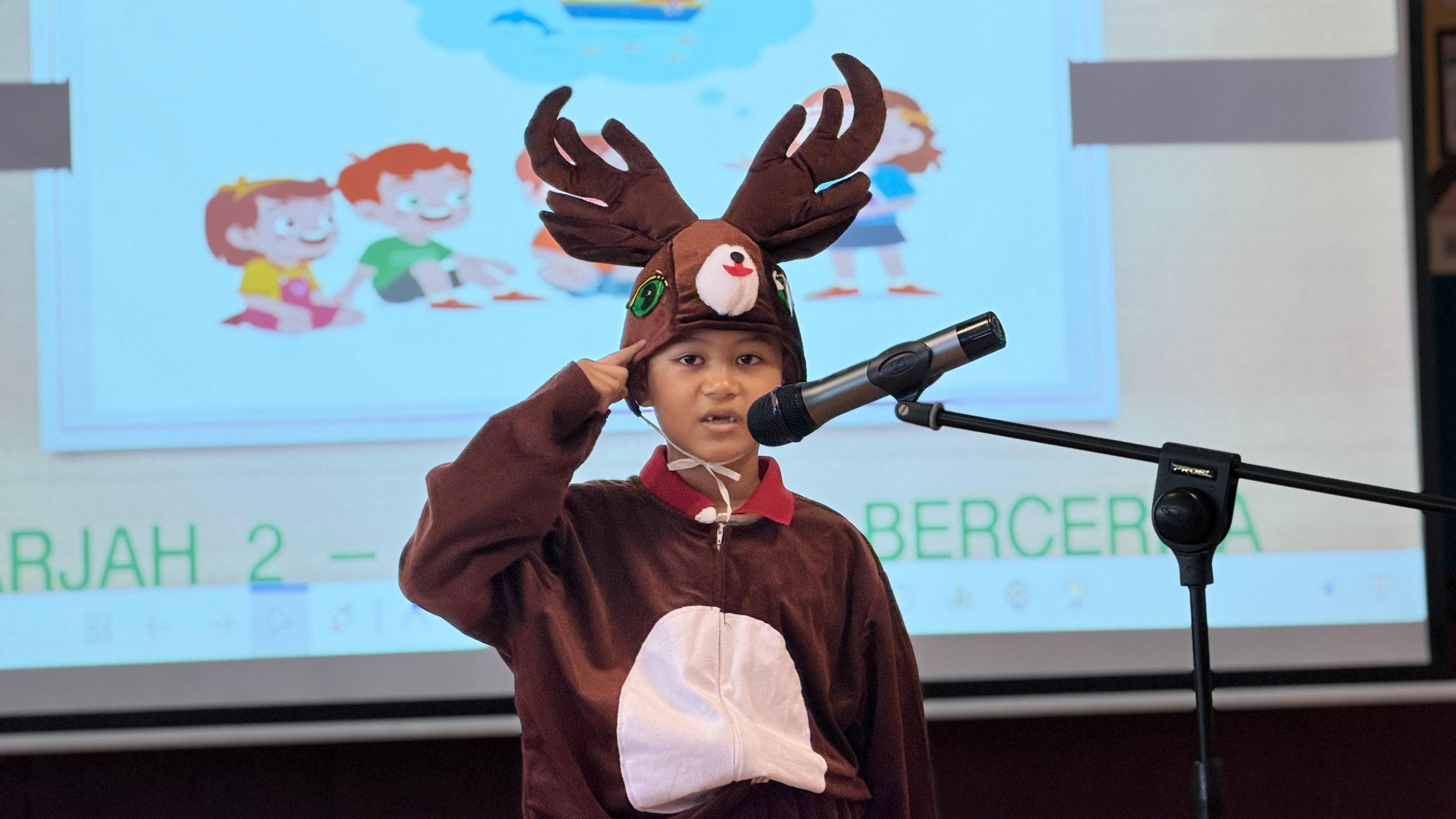 A student dressed as a deer reading a story through a microphone