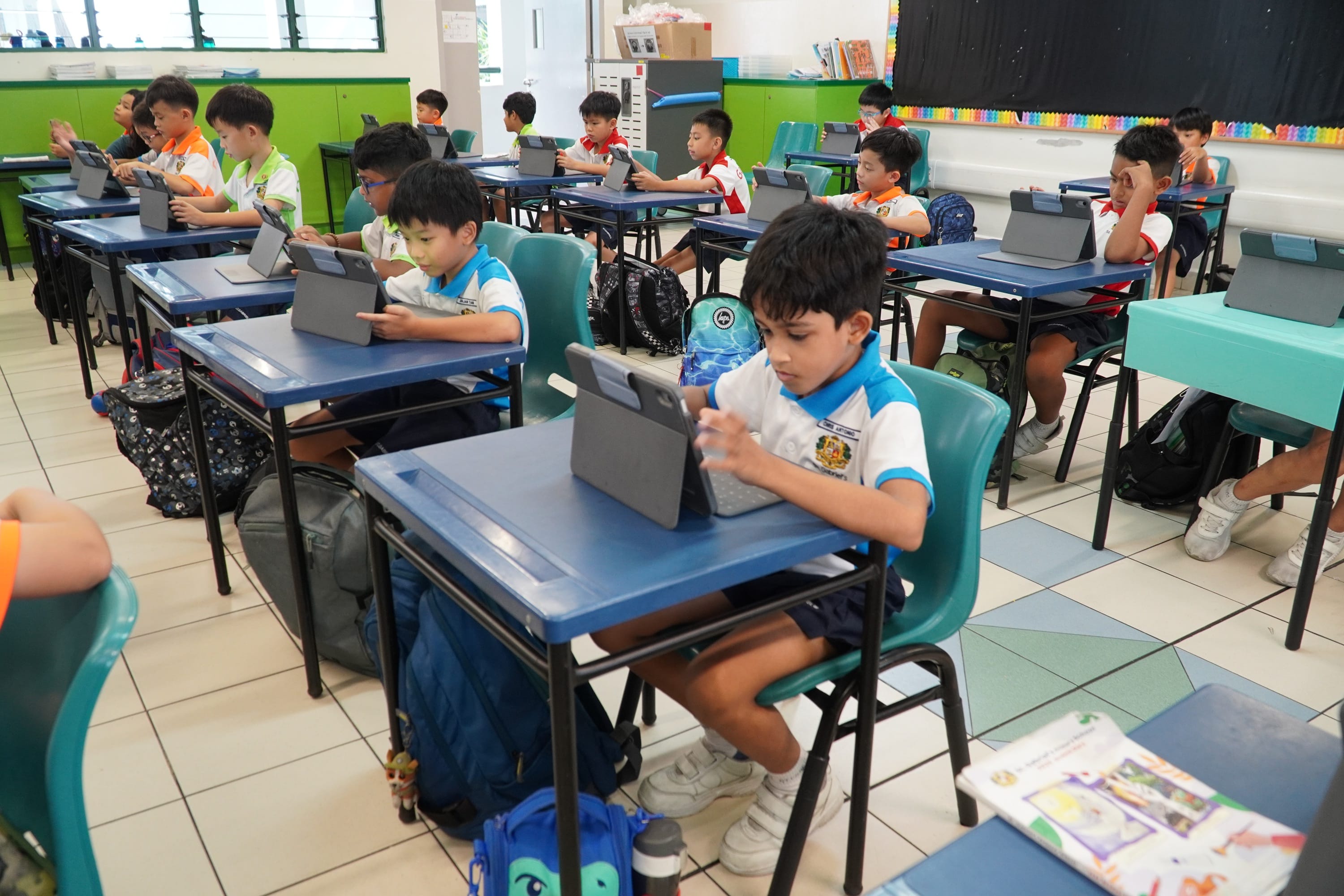 Students sitting on the chair working with an iPad on the table in front of them