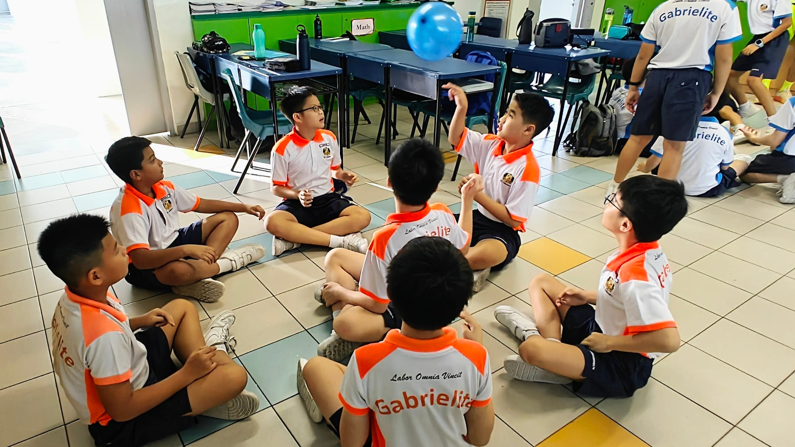Students playing with a balloon sitting down on the floor