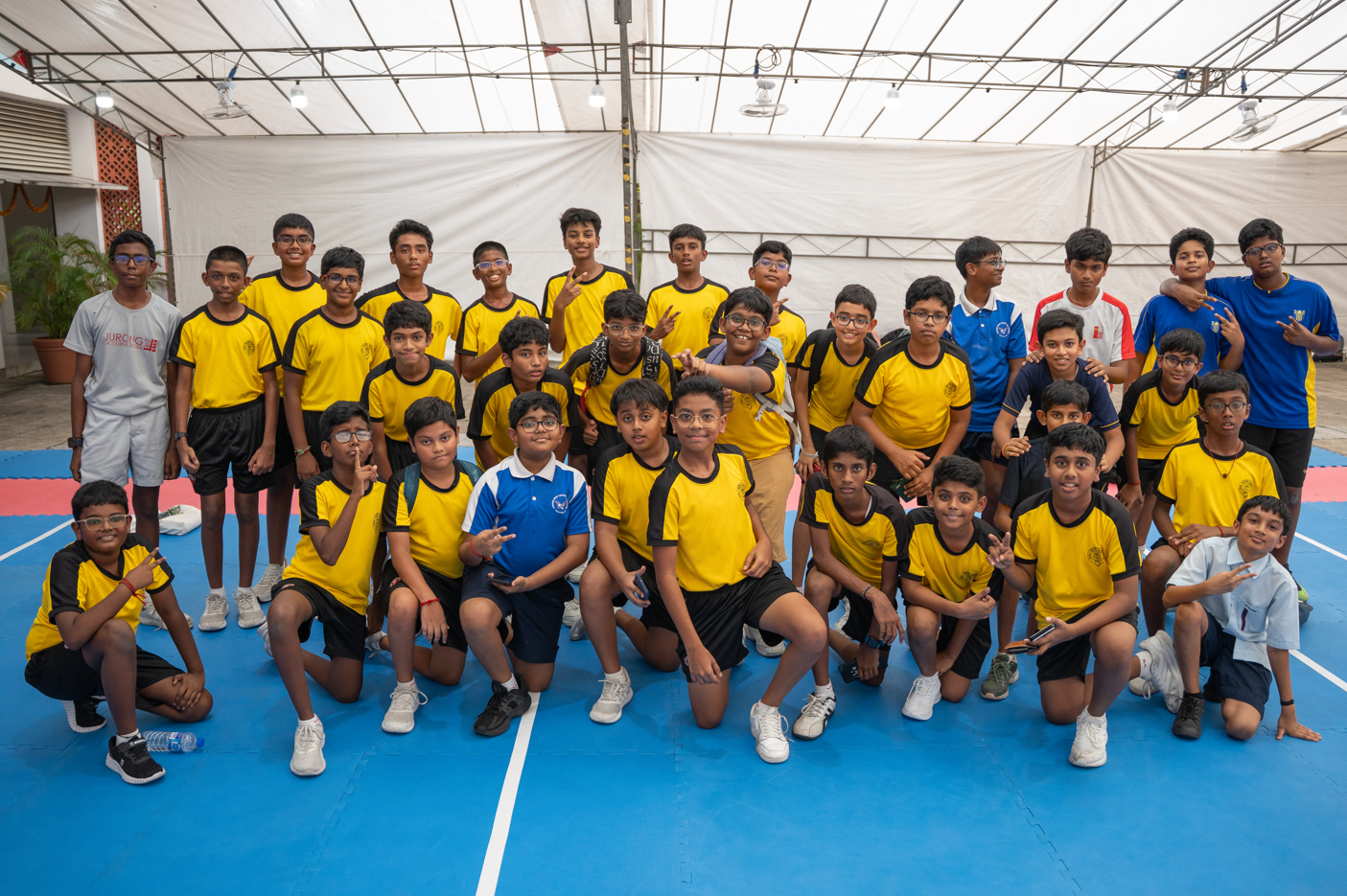 Group of boys in yellow sports jerseys pose on an indoor court under a covered roof.