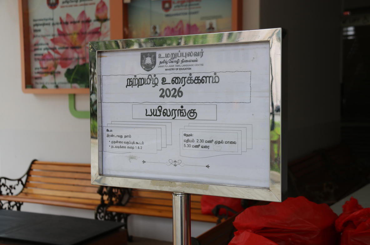 A framed Tamil language notice for Umar Pulavar Tamil Language Centre showing event details for 2026 on a stand.